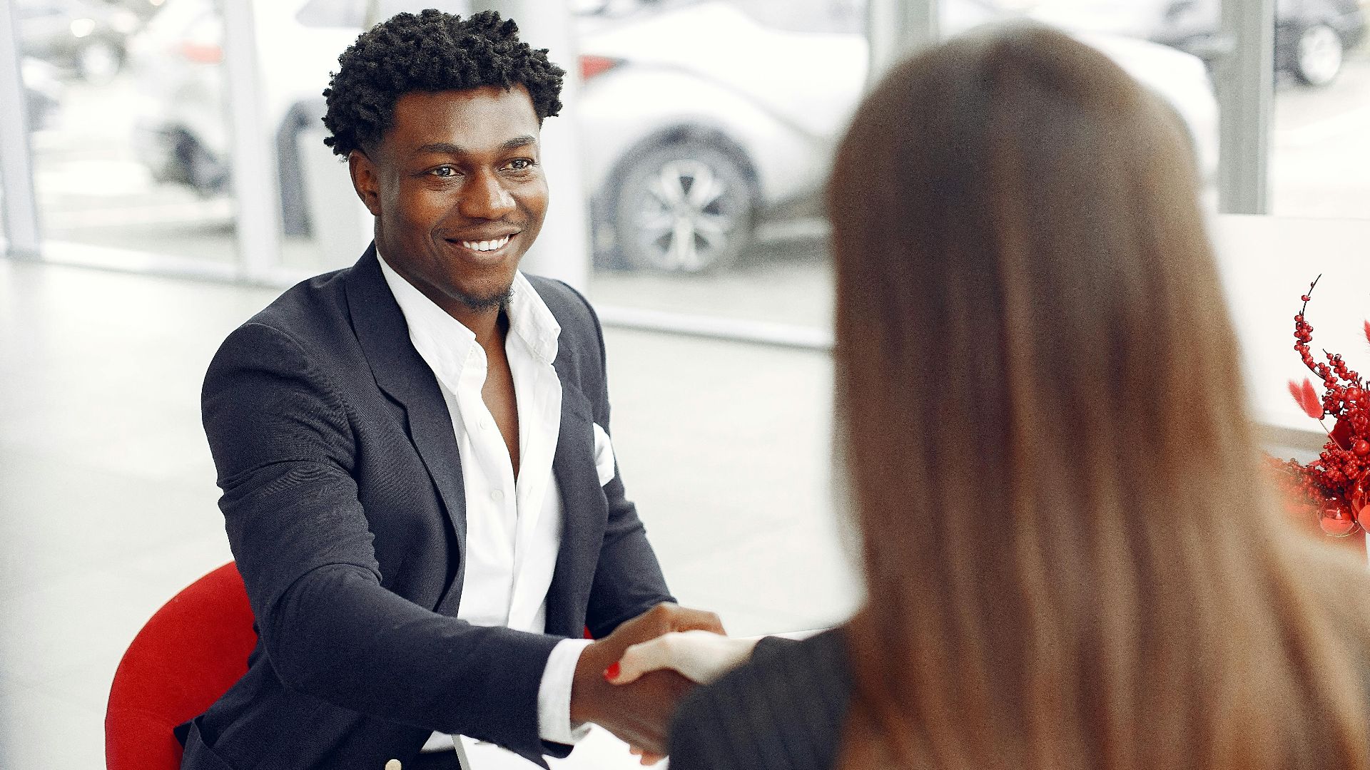 Cheerful happy African American customer in formal elegant suit shaking hands with female dealer after signing papers while smiling and looking at each other