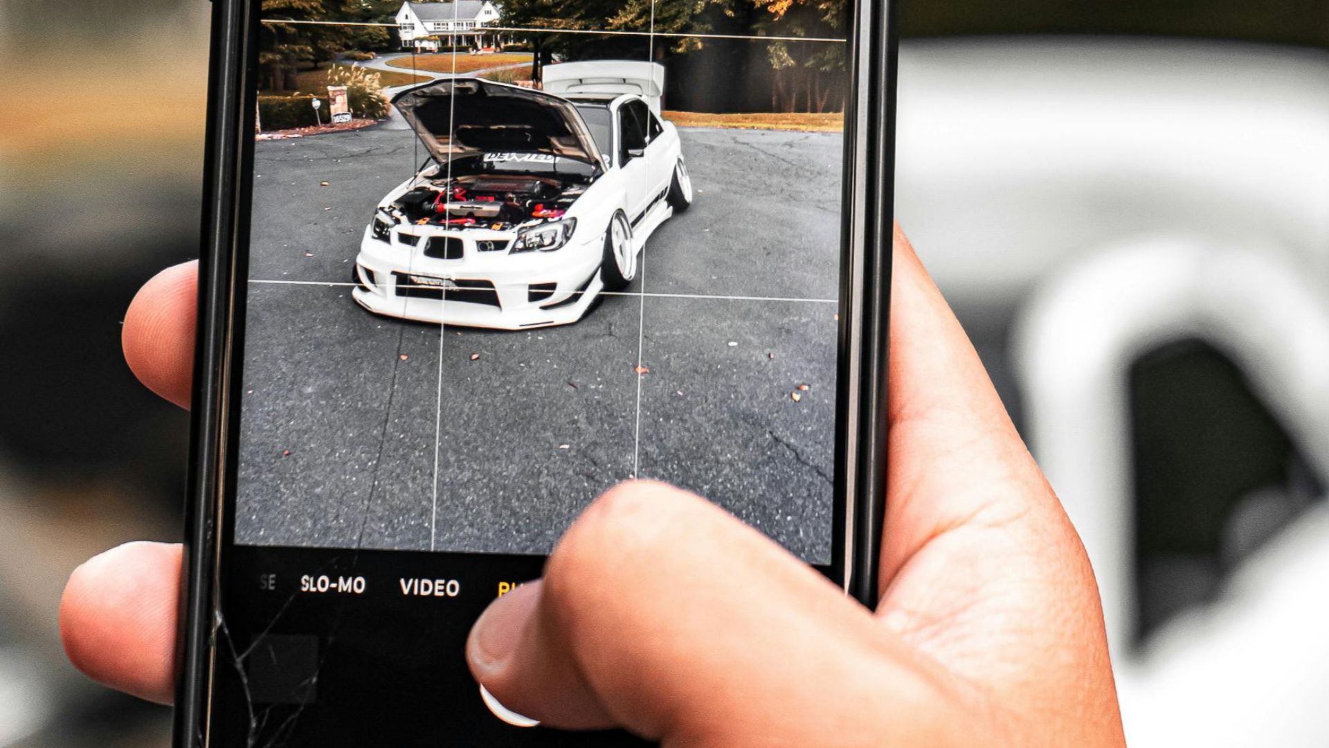 Person photographing a white car outdoors with a smartphone, showing technology and leisure.