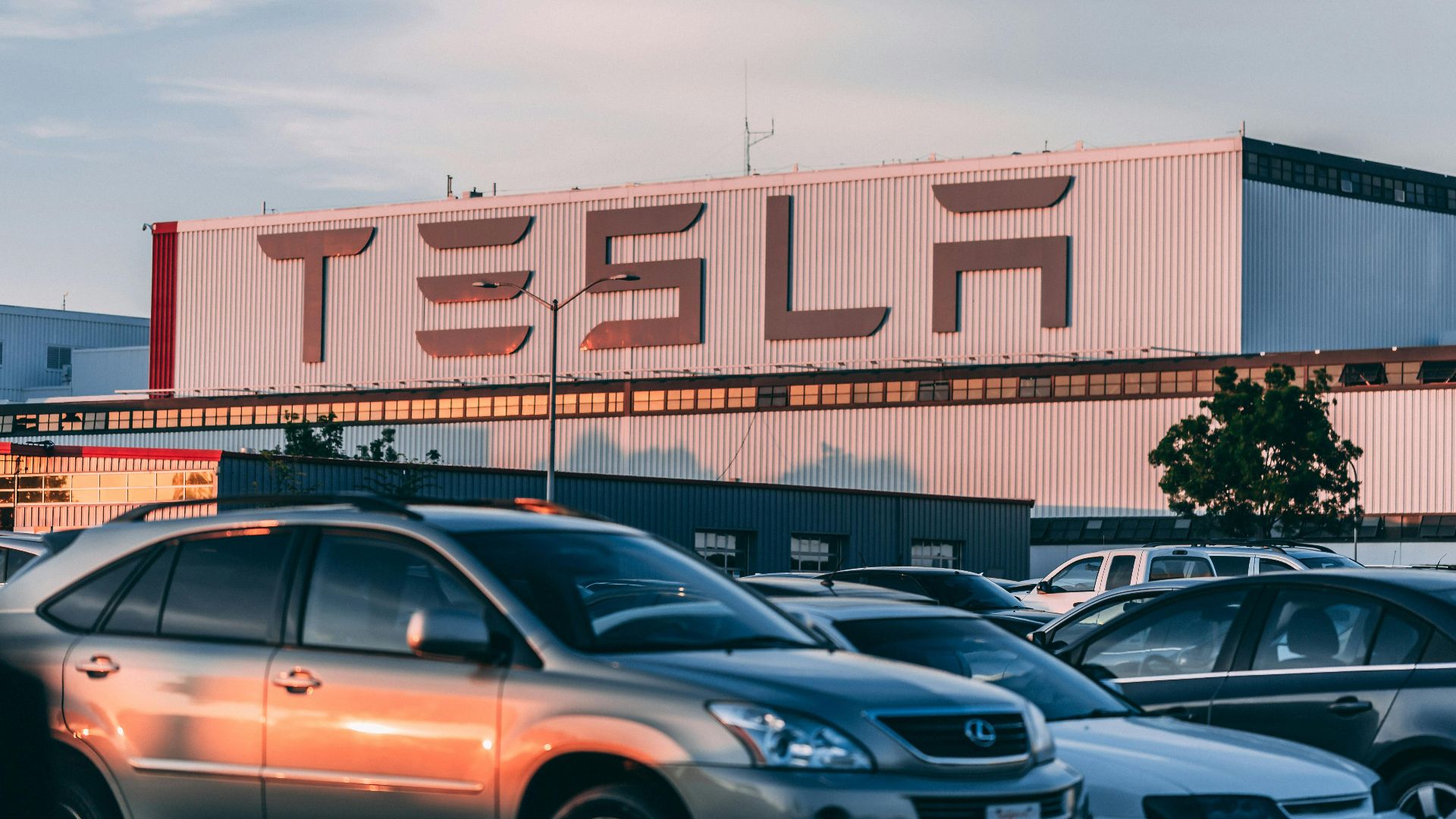 Tesla factory with parked cars during sunset, showcasing modern automotive industry vibes.