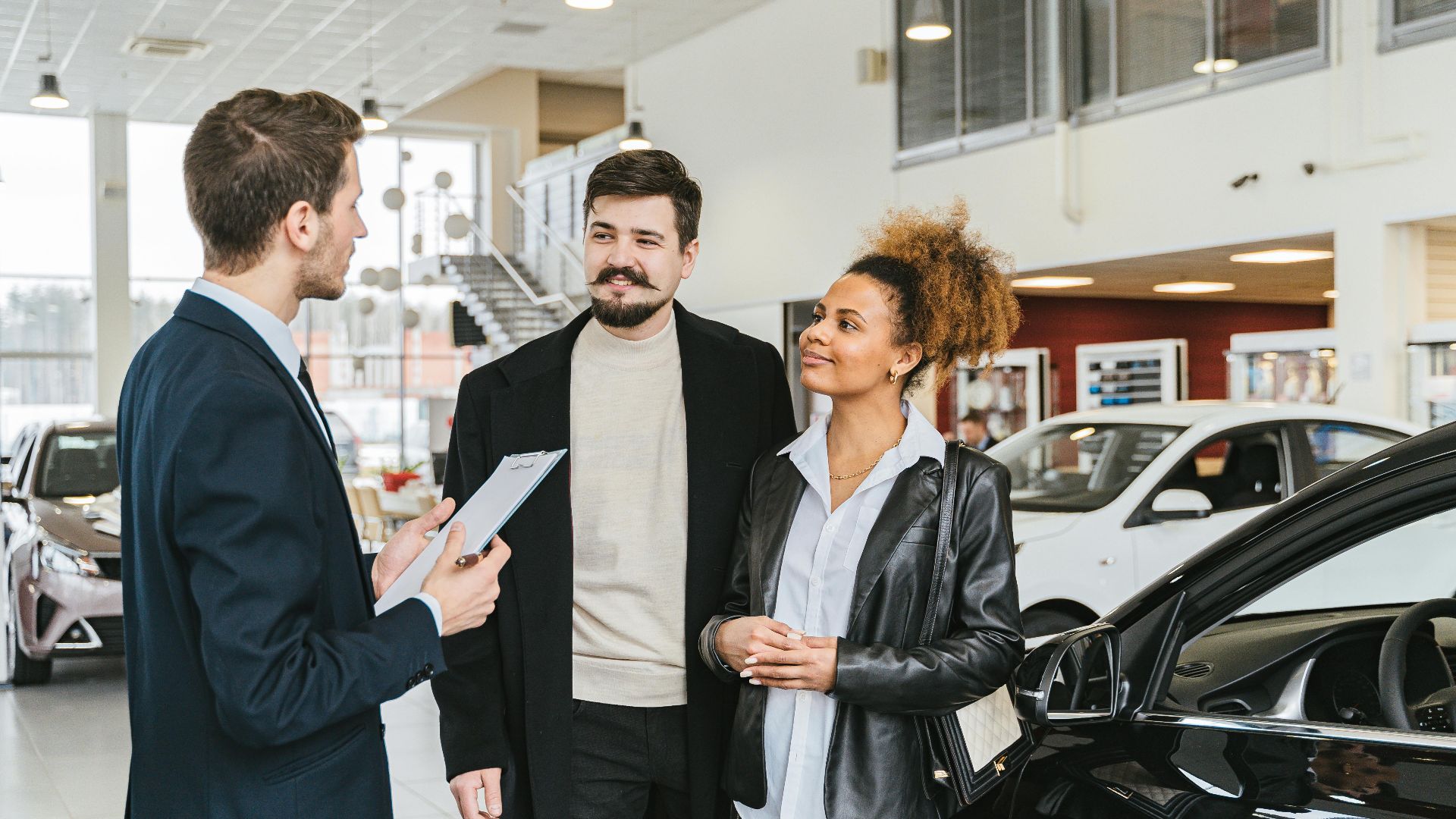 Couple discussing car purchase with salesman at indoor dealership, engaging conversation.