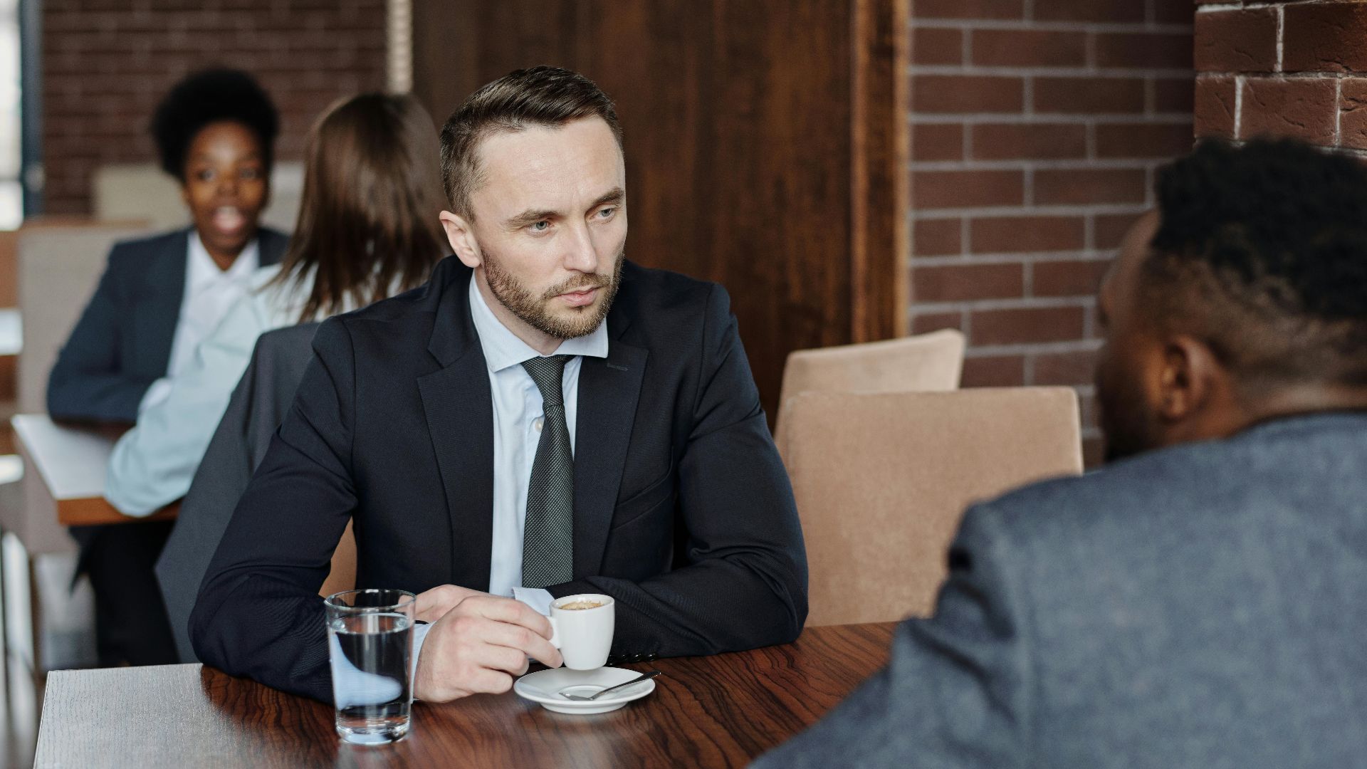 Two businessmen in suits discussing over coffee during a meeting in a café.