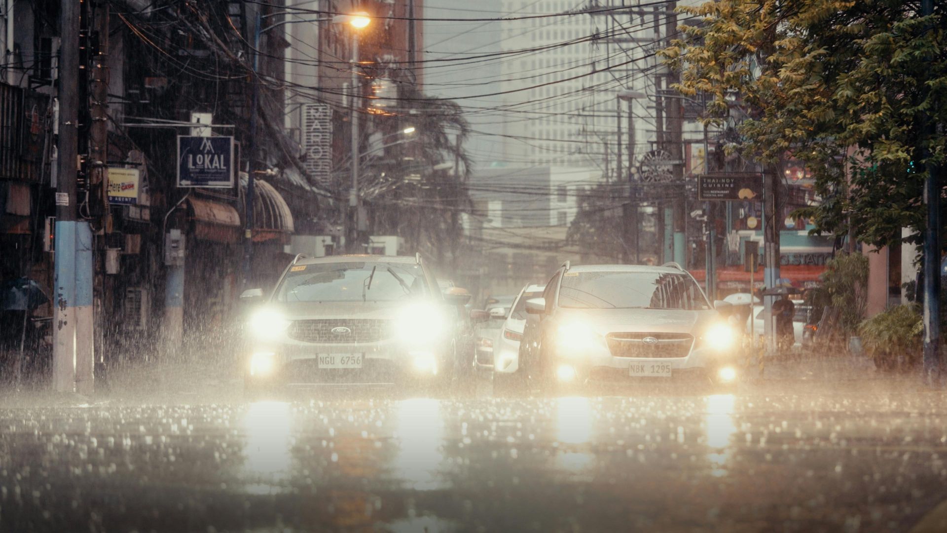 Nighttime urban street view featuring cars driving through heavy rain and reflections.