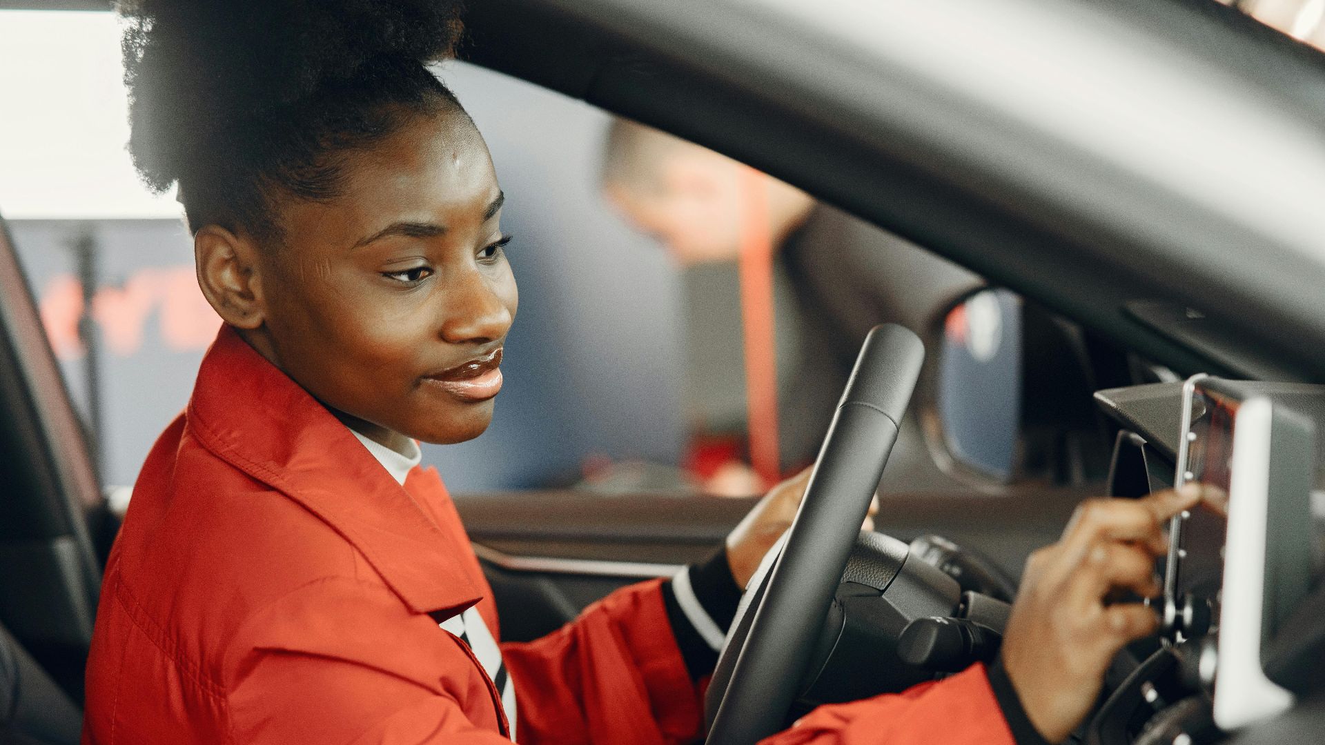 Young woman in red coat using touch screen in car interior.