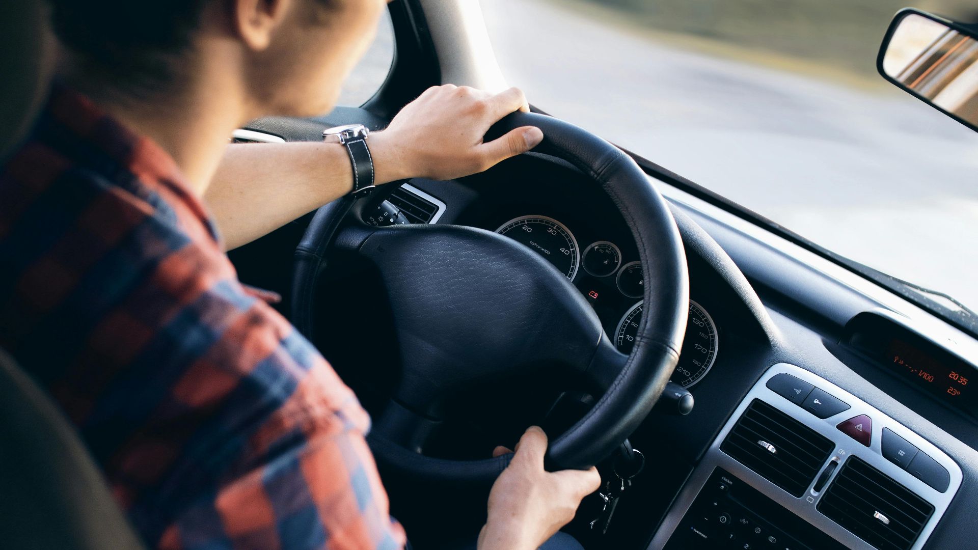Close-up view of a man driving a modern car, showing dashboard and steering details.