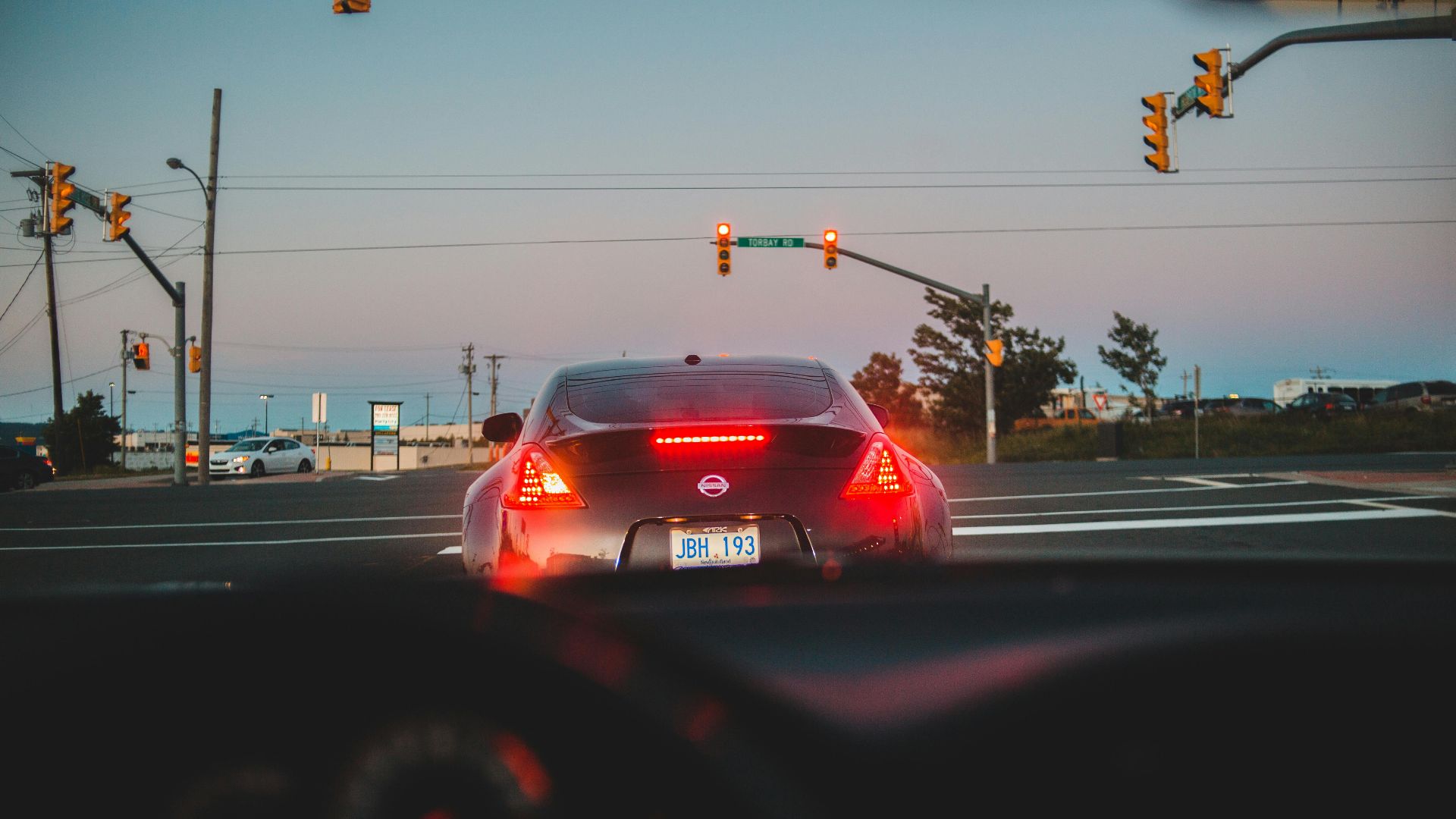 From windshield view of back of modern black car with glowing taillights on road intersection at dusk
