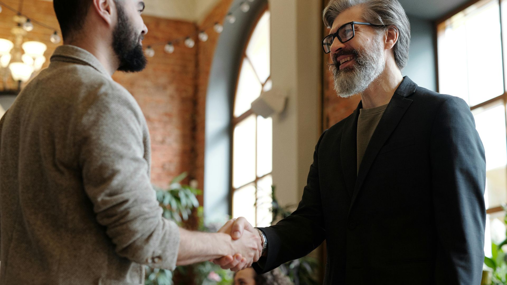 Two businessmen smiling during a handshake in a modern office setting, symbolizing success and partnership.