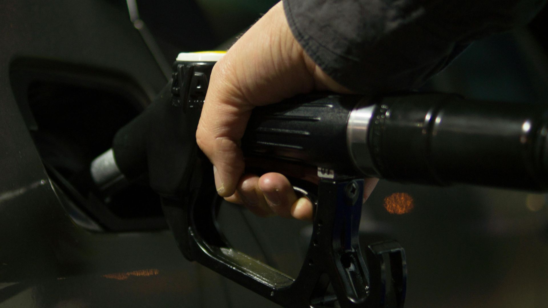 Close-up of a person refueling a car at a gas pump during night.