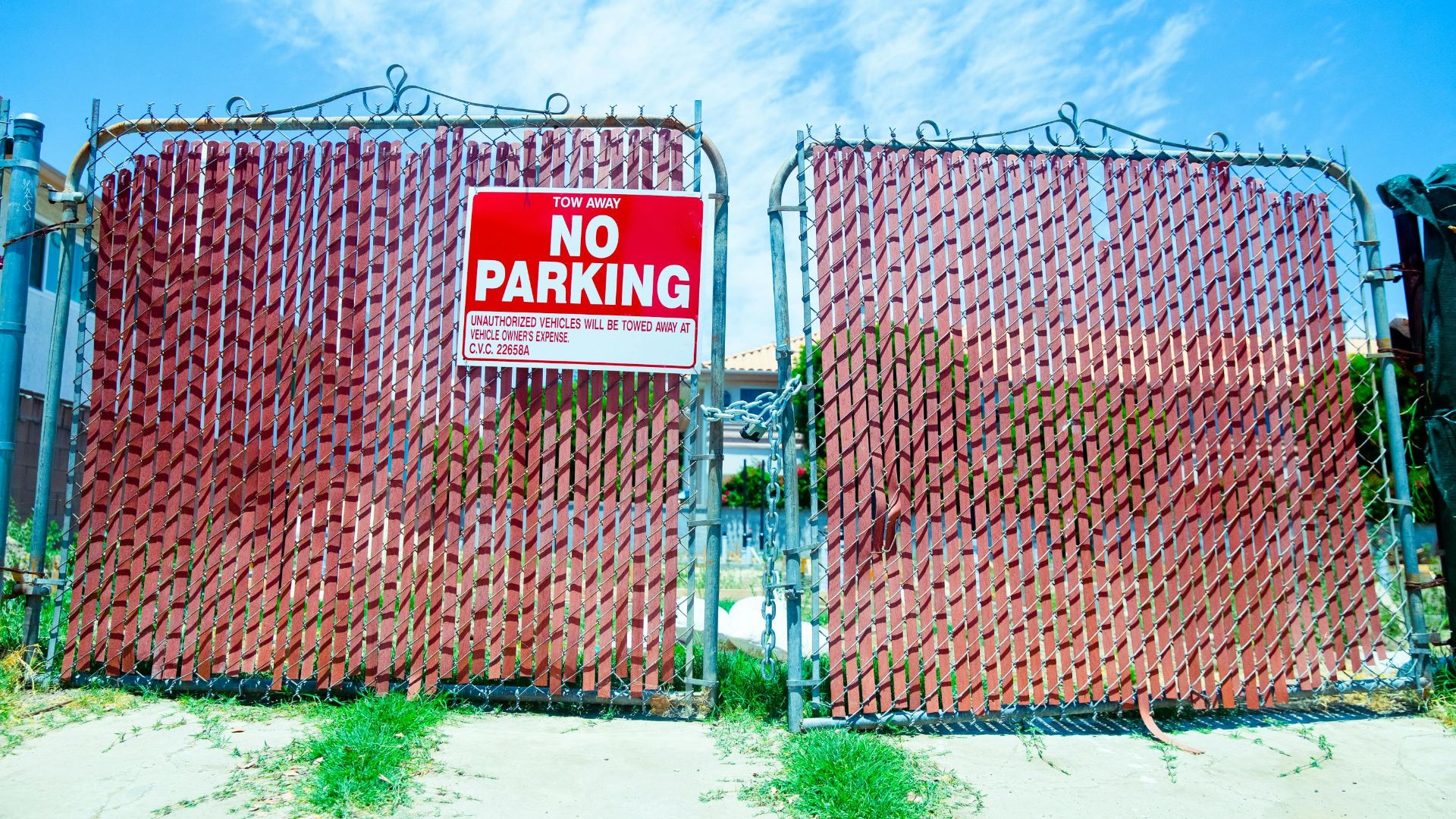 Red 'No Parking' sign on a metal gate with a vibrant blue sky background.