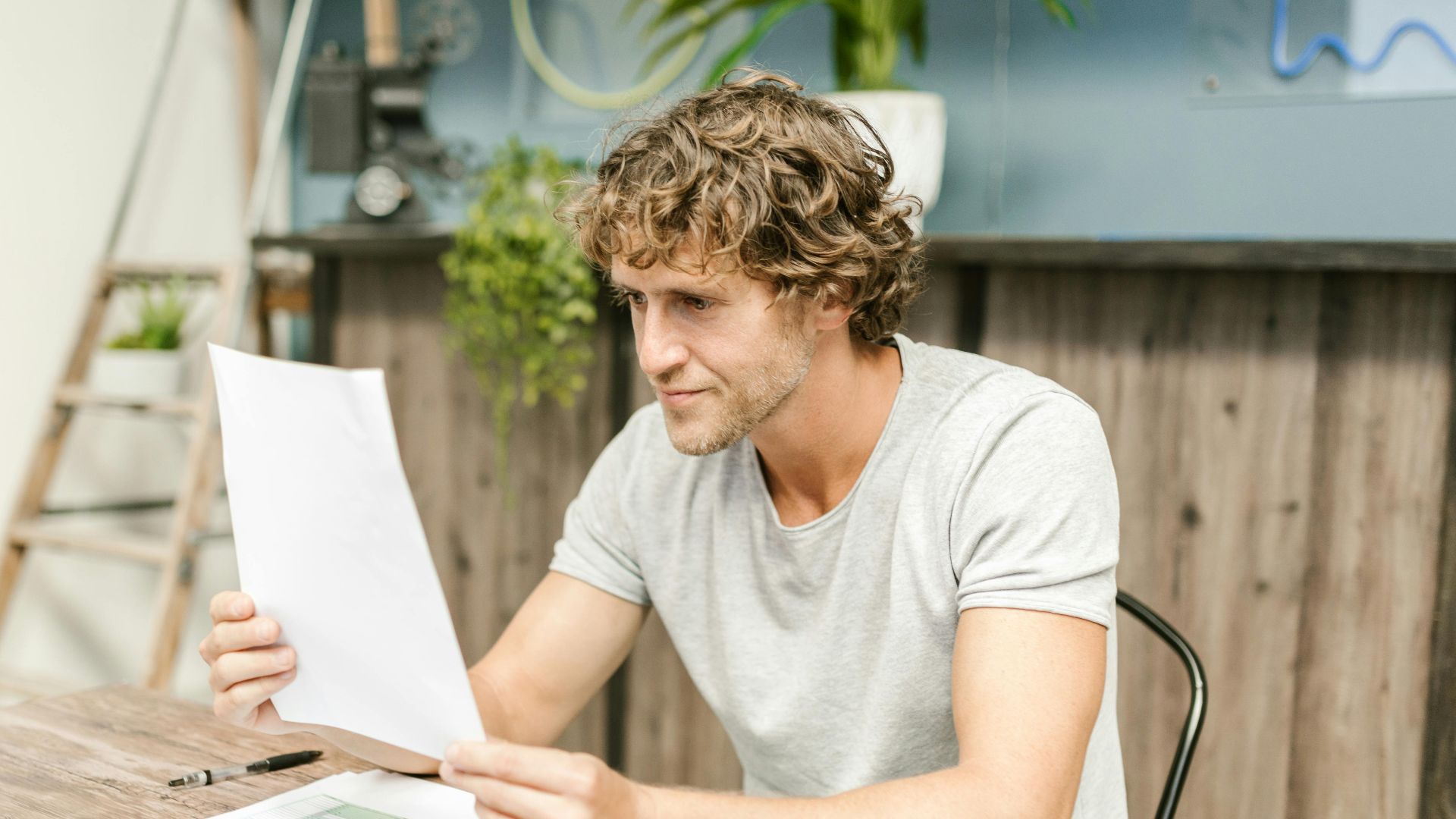 A man with curly hair evaluates documents at a desk, highlighting focused work in a professional setting.