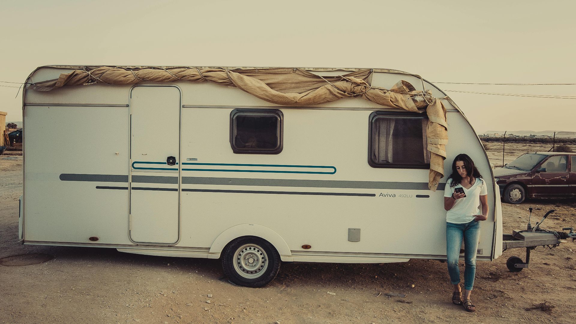 A woman stands by a camper van in a serene outdoor setting during sunset.