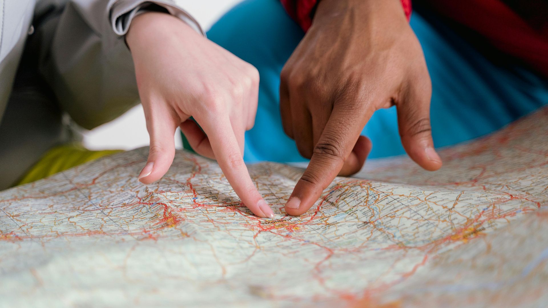 Close-up of diverse hands pointing at a paper map, symbolizing travel planning and navigation.