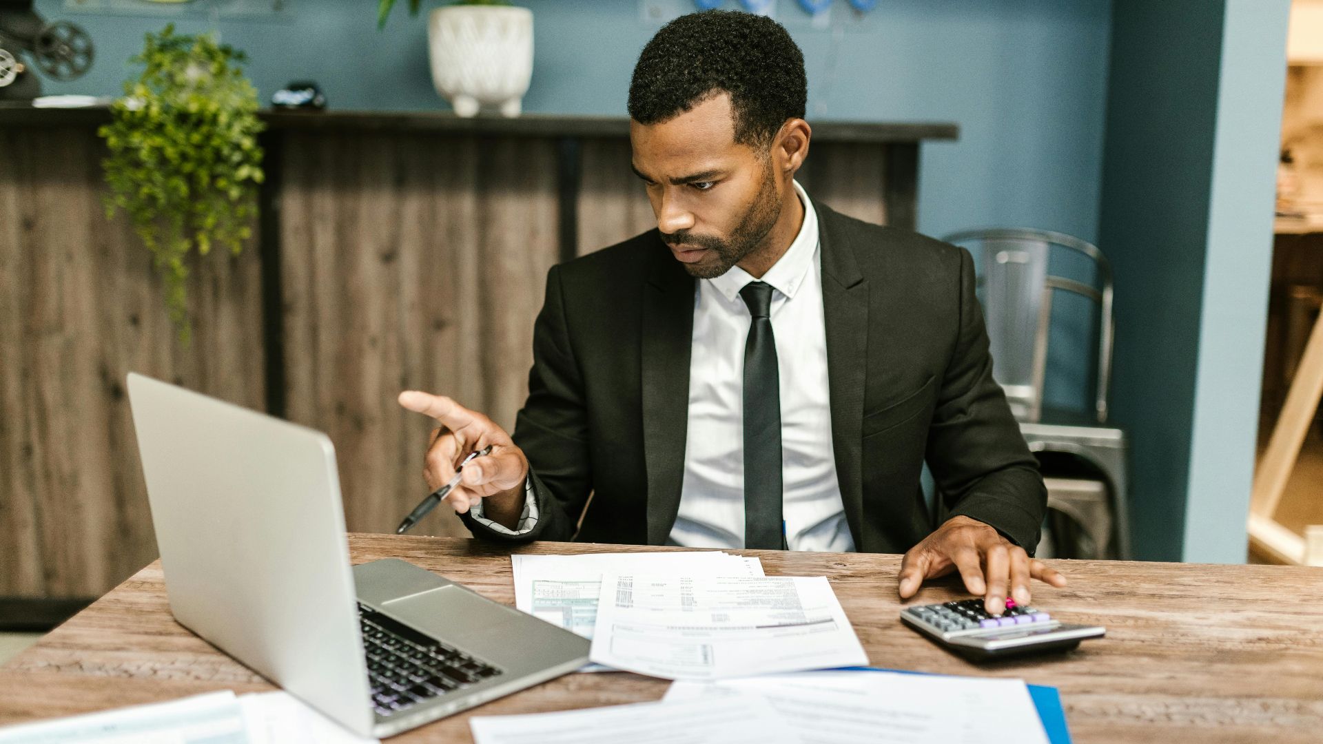 Professional man in a suit using a laptop and calculator in an office setting.