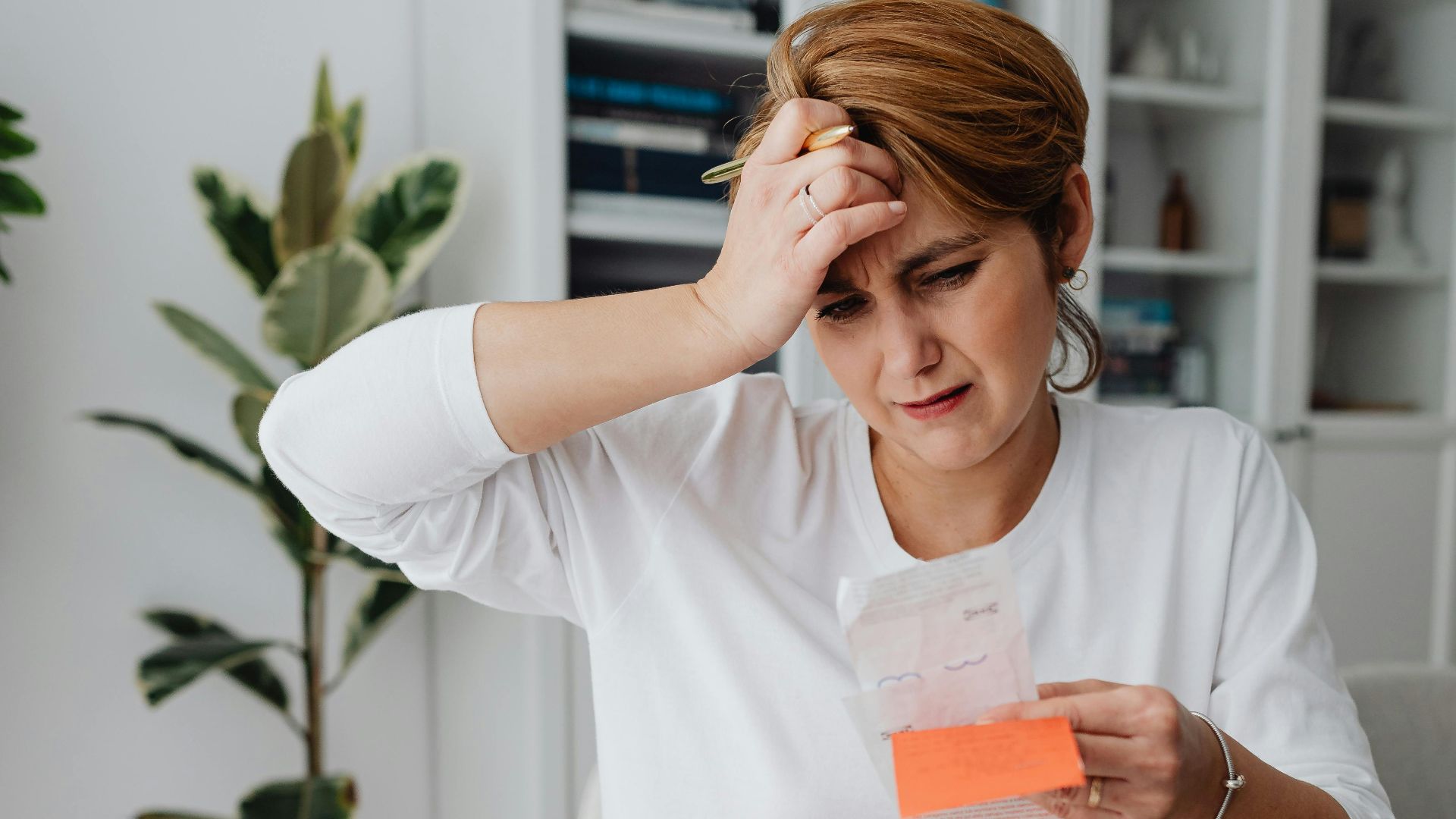 A businesswoman in an office looks frustrated while reviewing bills and finances with a laptop, displaying anxiety.