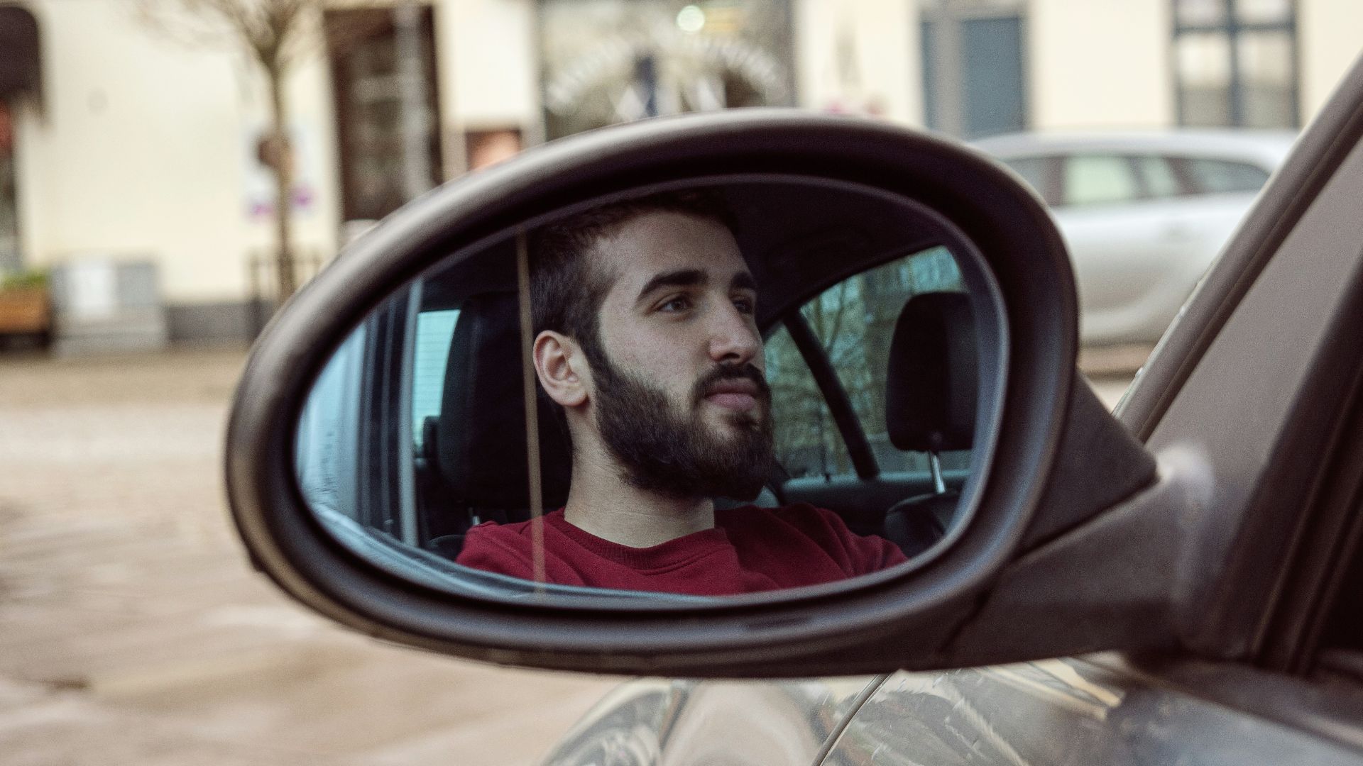man in red crew neck shirt looking at car side mirror
