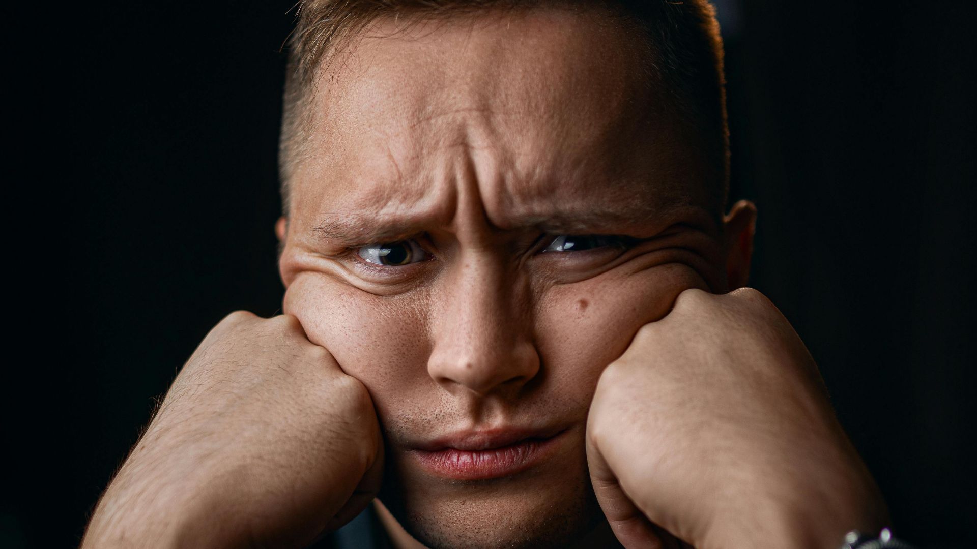 Unhappy male in formal outfit with wristwatch leaning on fists while looking at camera