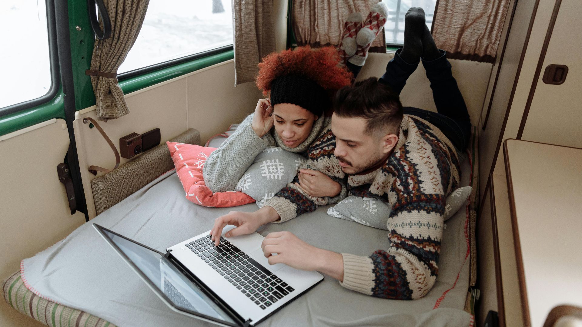 Couple enjoying leisure time in campervan, using laptop in a cozy interior setting.