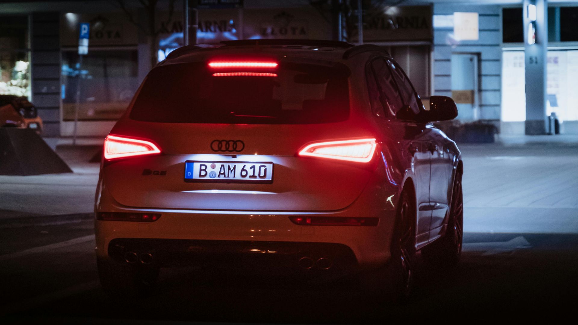 Hatchback car parked at night with glowing tail lights in an urban setting.