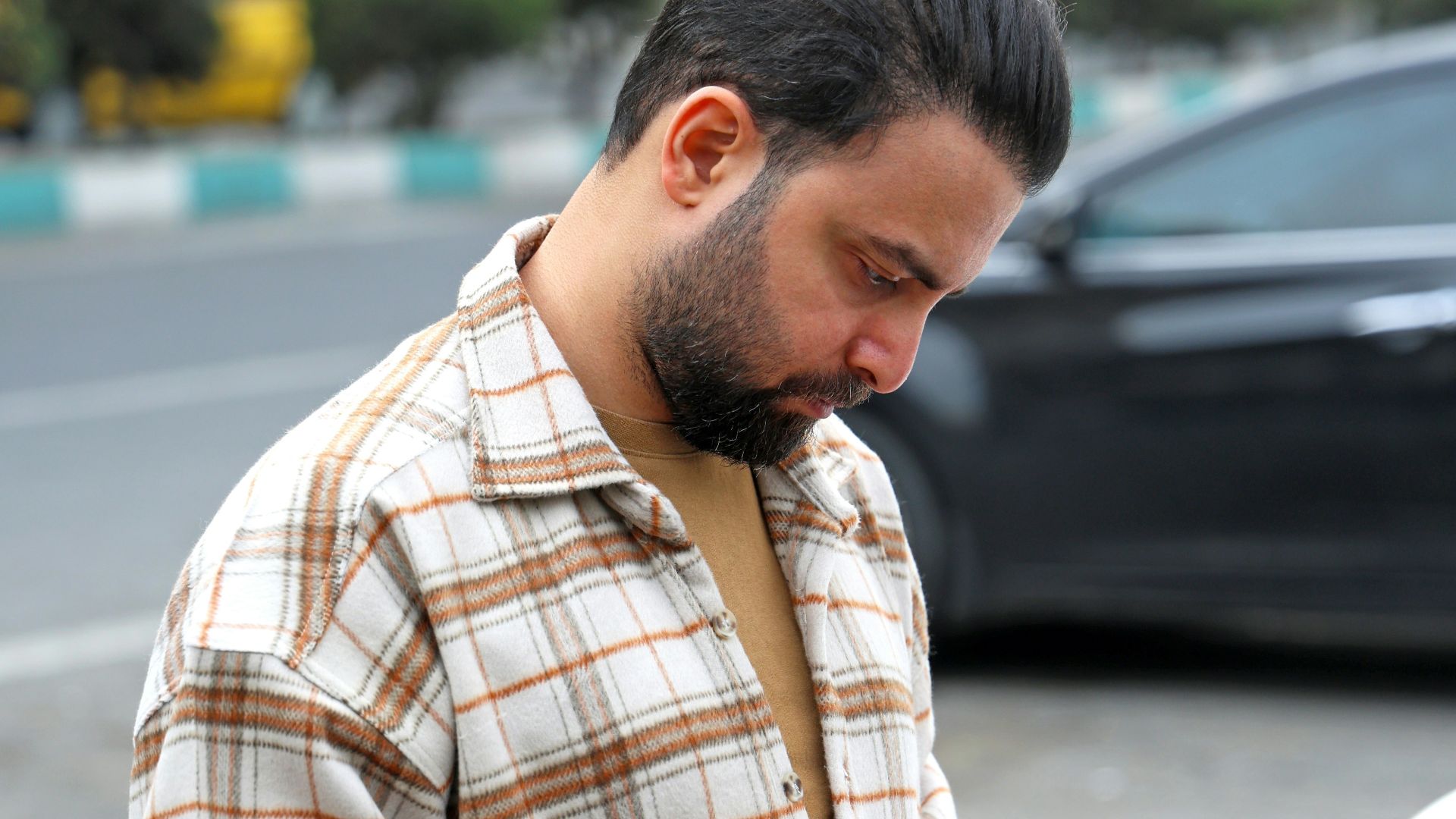 Man in plaid shirt looking at his phone outside phone.