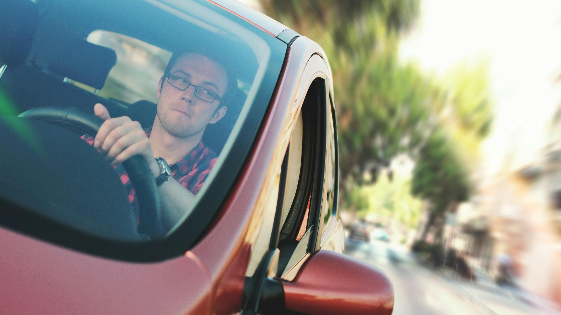 A man driving fast through a city street in a red car, showcasing motion and focus.
