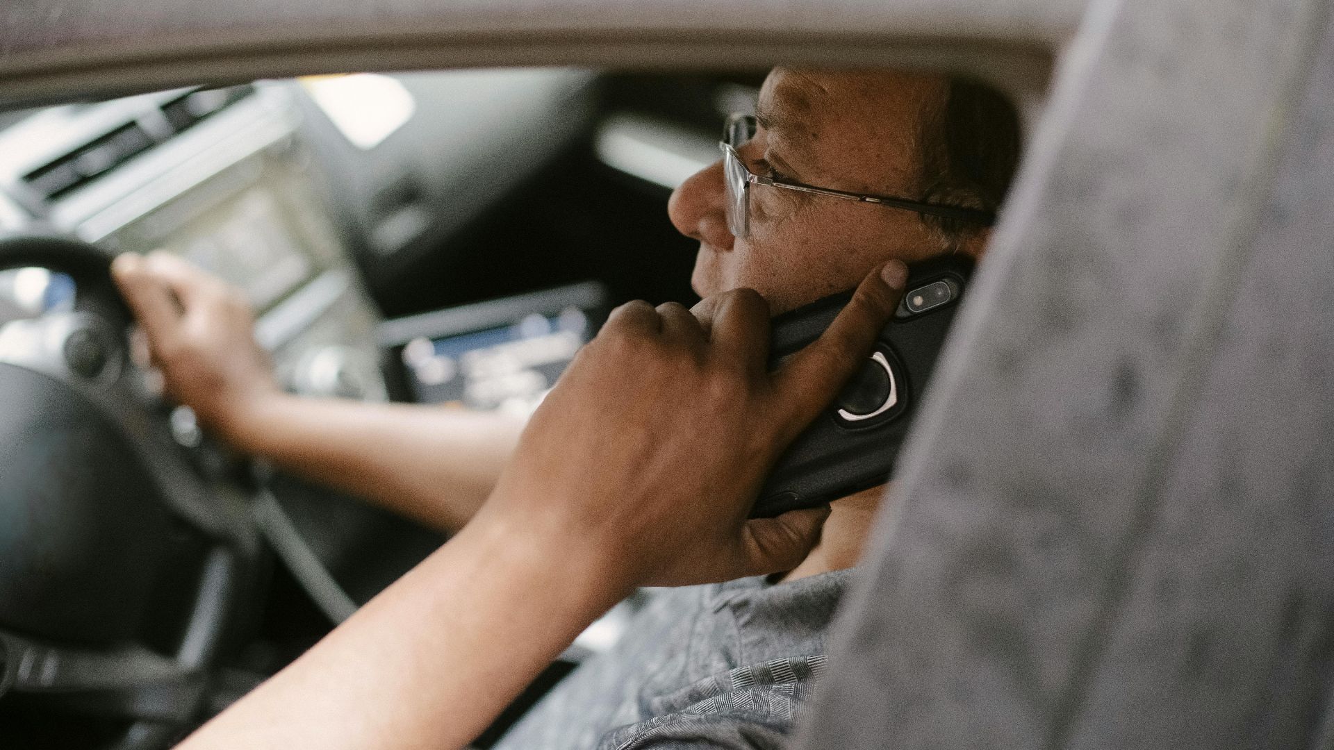 Side view of a taxi driver talking on a phone while driving through the city.