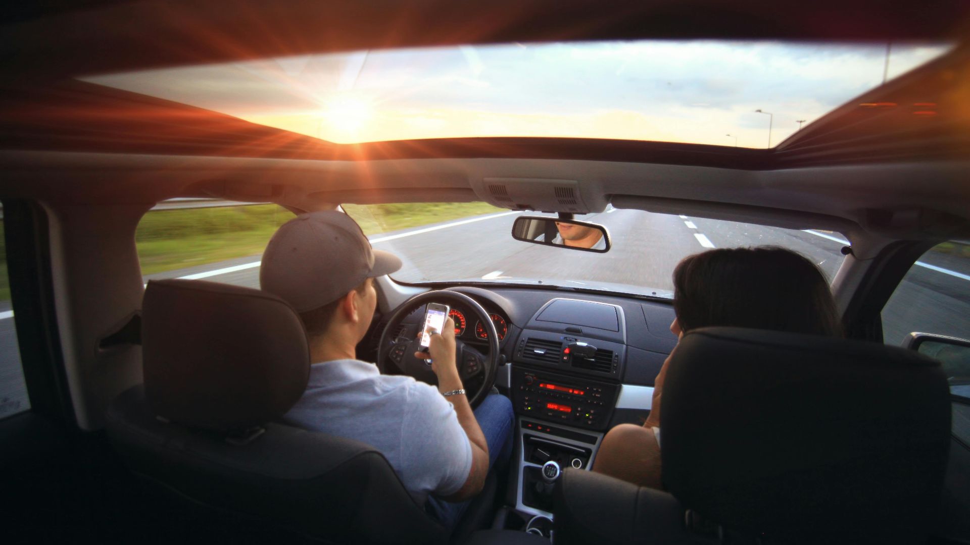 Driver using phone while driving at sunset with passenger in vehicle.