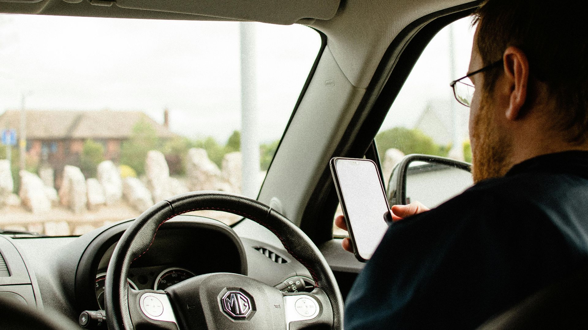Person in a car using a smartphone with a focus on dashboard and steering wheel.