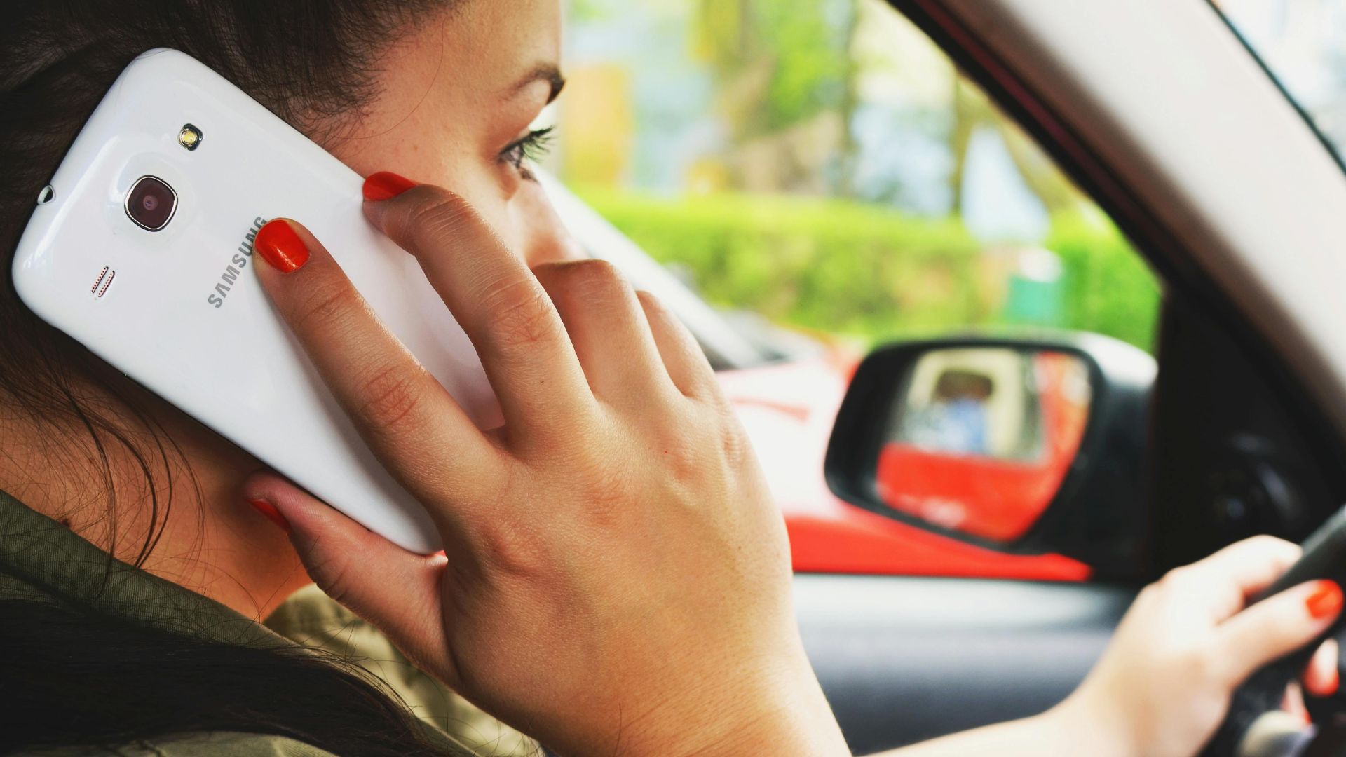 Close-up of a woman driving a car while talking on a smartphone, highlighting road safety concerns.