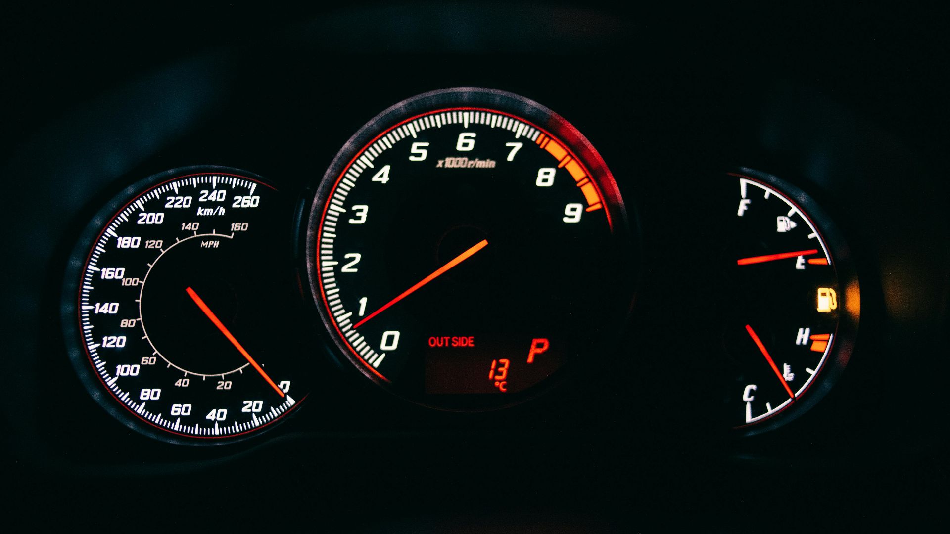 Close-up of a car dashboard showcasing speedometer and gauges with illuminated dials against a black background.