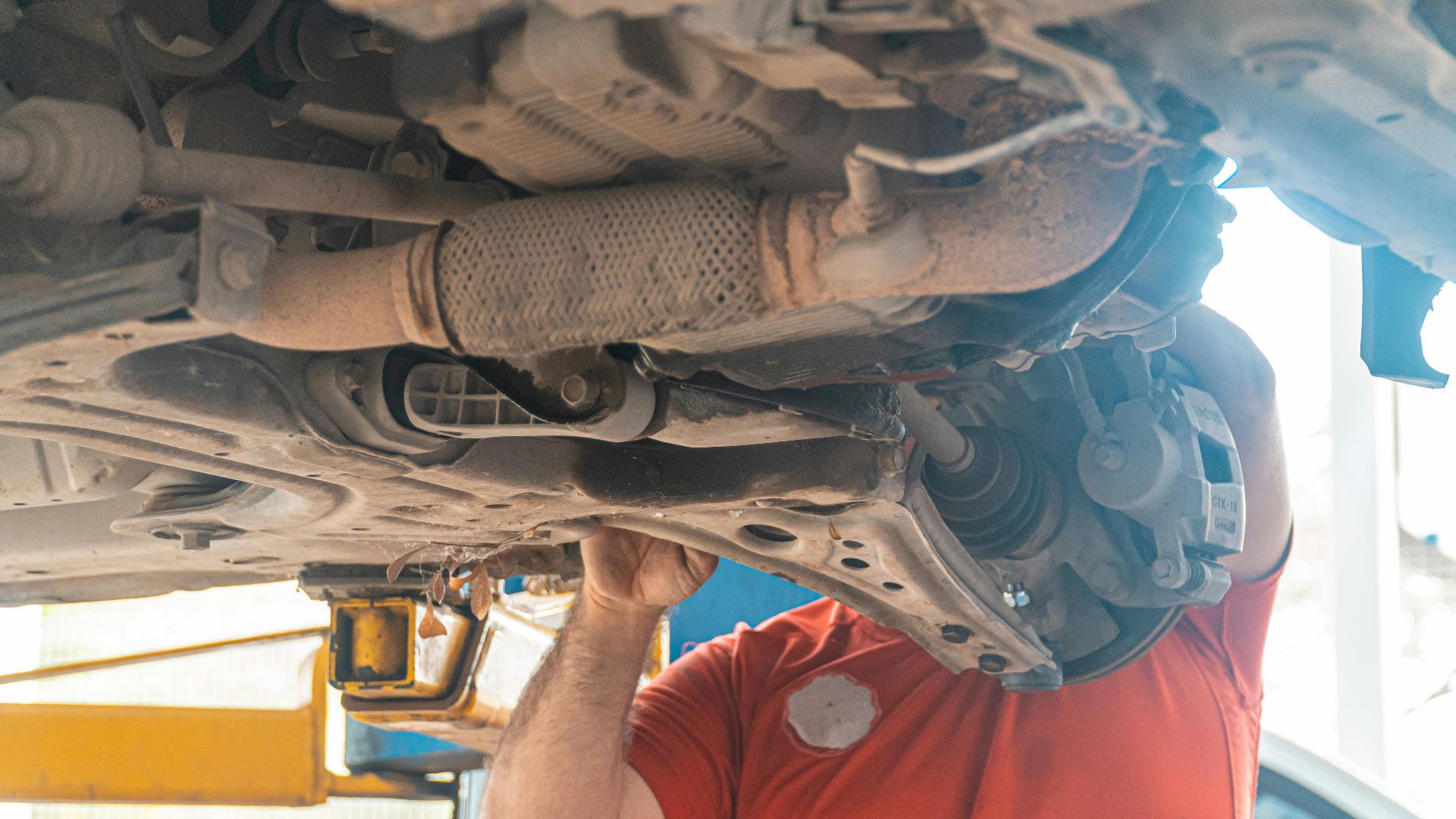 Mechanic working under a vehicle, inspecting the undercarriage in a repair garage, ensuring safety and performance.