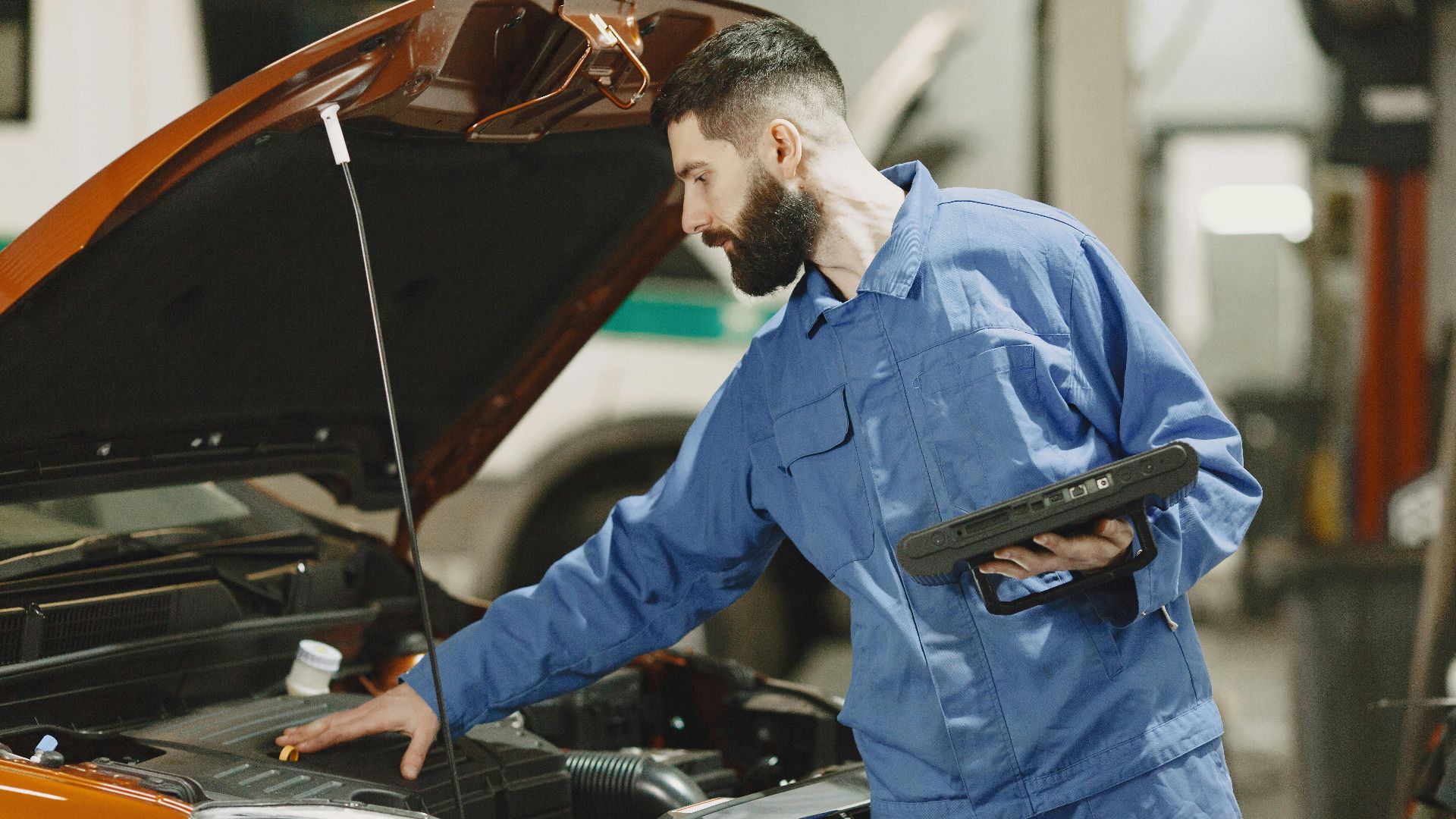 Professional mechanic examining a car engine under an open hood in a garage setting.