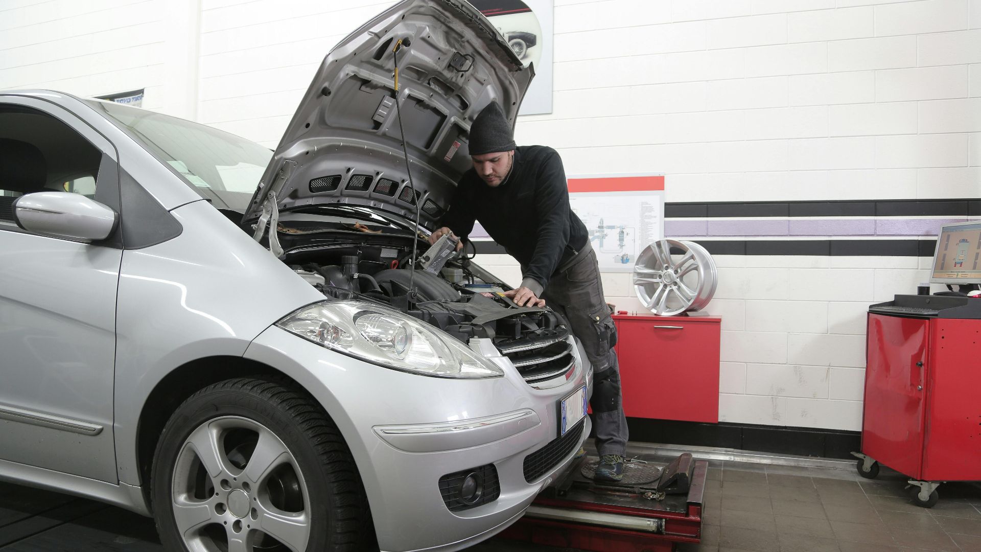 A mechanic checks a car engine for maintenance in a garage setting.
