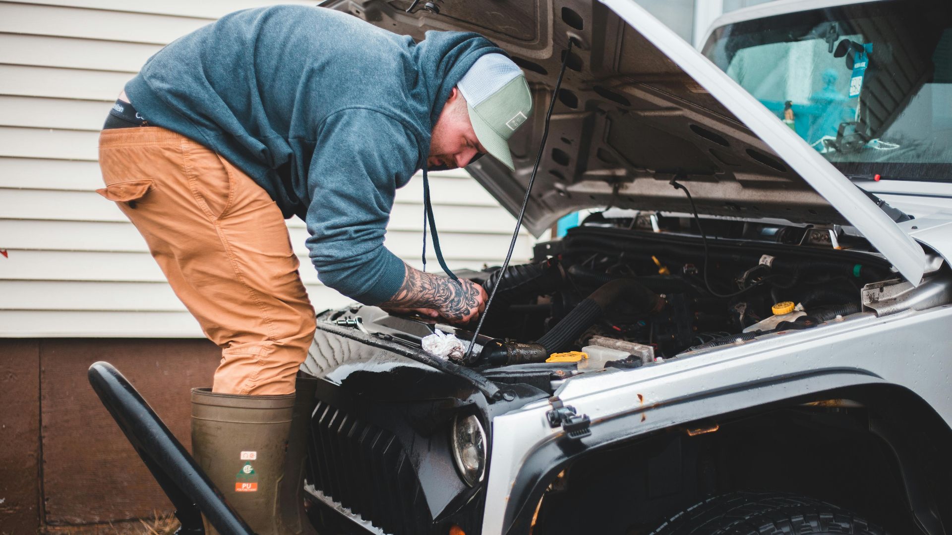 A man inspects and repairs a car engine outside, showcasing automotive maintenance and repair skills.