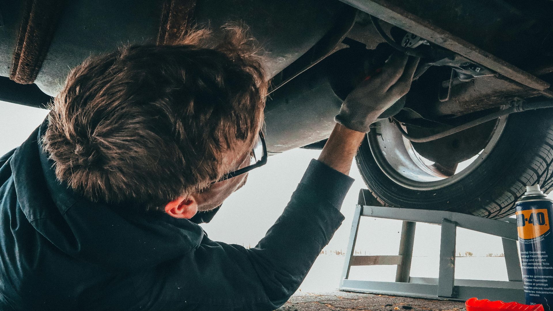 Mechanic skillfully repairing car undercarriage in outdoor setting with tools.
