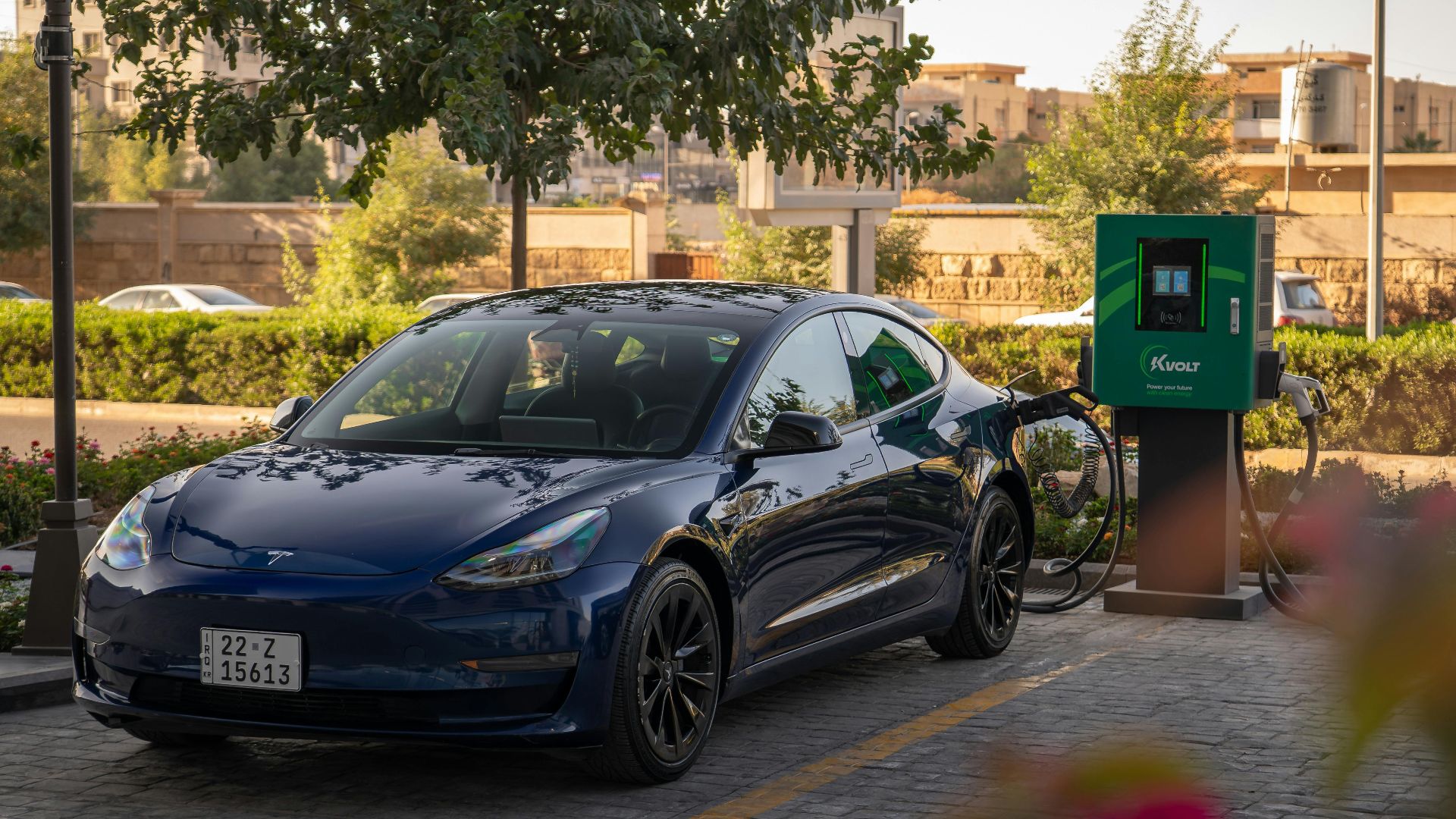 Tesla Model 3 charging at an urban electric vehicle station during daytime.