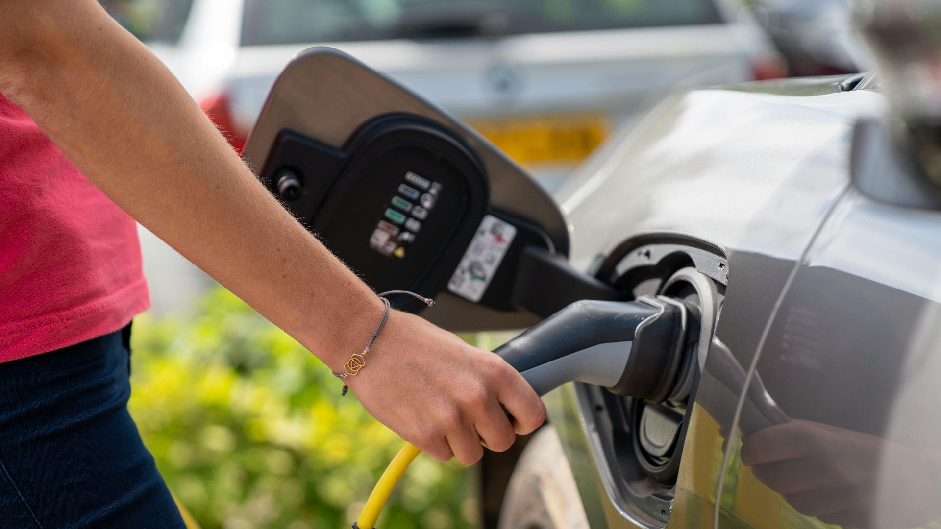 Close-up of a person plugging in an electric car at a charging station outdoors.