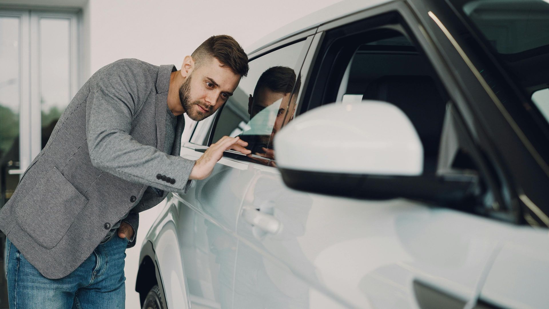 Man carefully examining a modern white car at a dealership showroom.