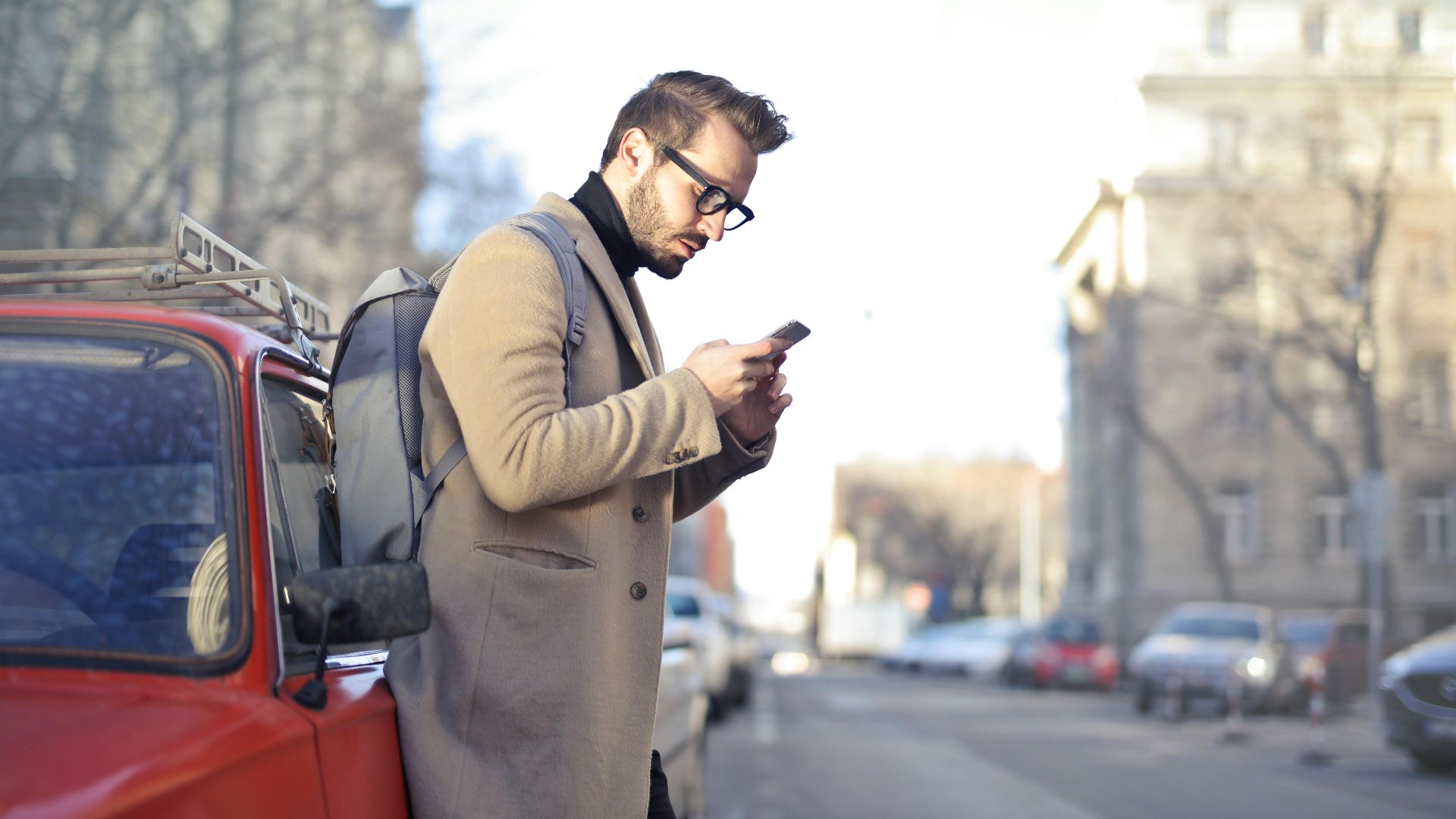 Man with backpack using smartphone on urban street in Budapest.