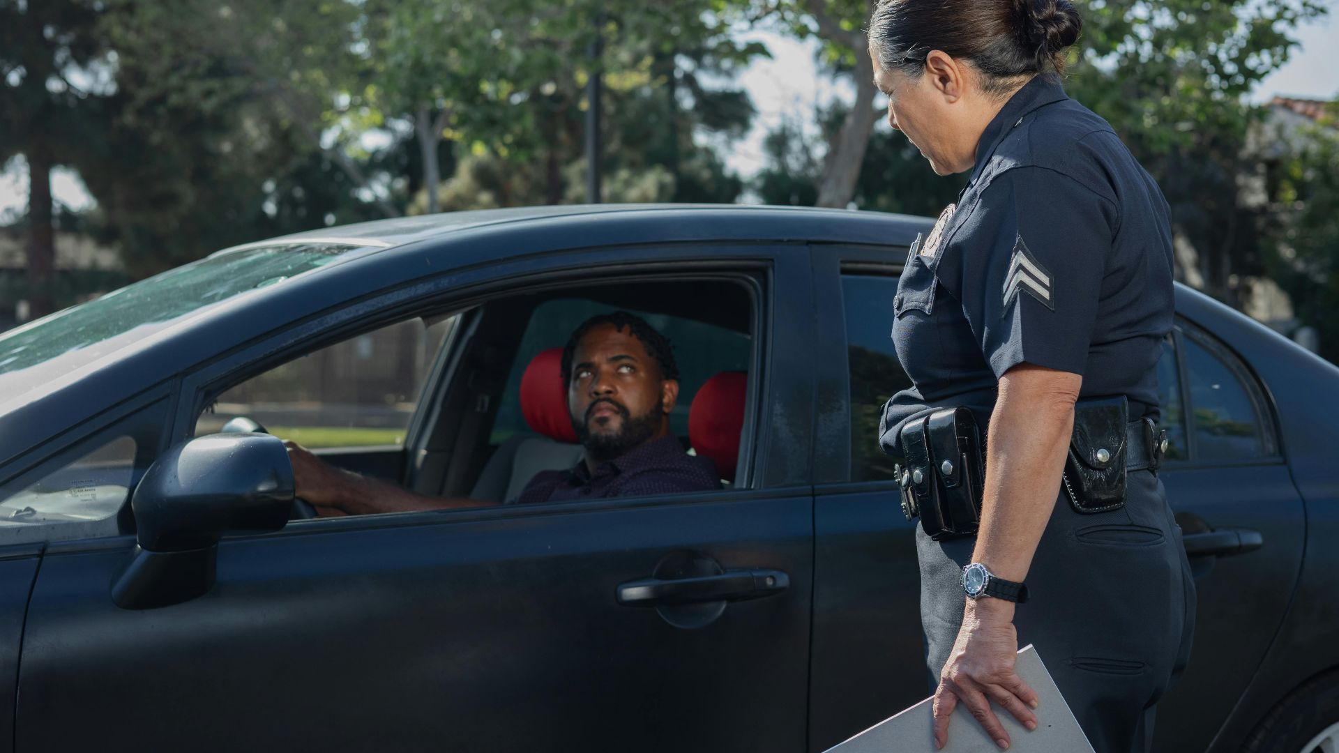 A policewoman discusses a traffic violation with a driver on a sunny day.