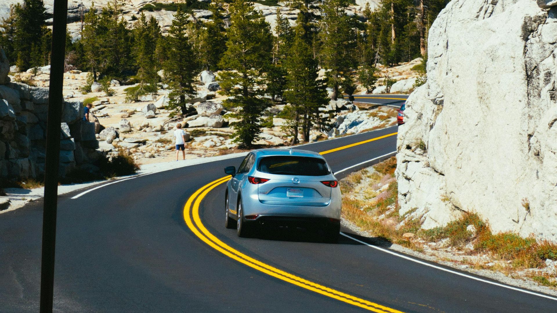 A scenic mountain road with curves and a car driving under a bright blue sky.