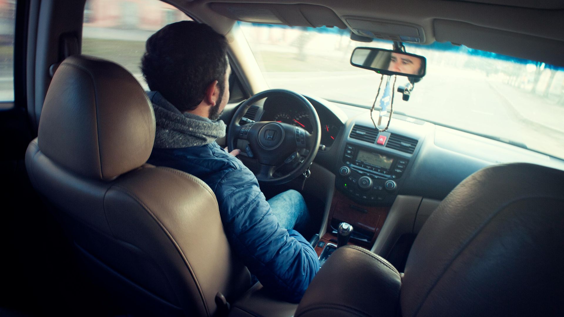 A man driving a car with focus on interior, dashboard, and steering wheel, captured from the backseat.