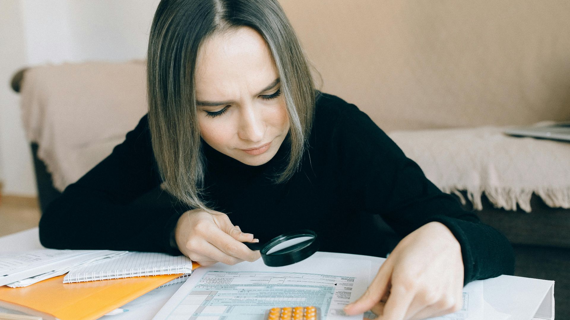 A focused young woman examines documents with a magnifying glass, highlighting attention to detail in accounting tasks.