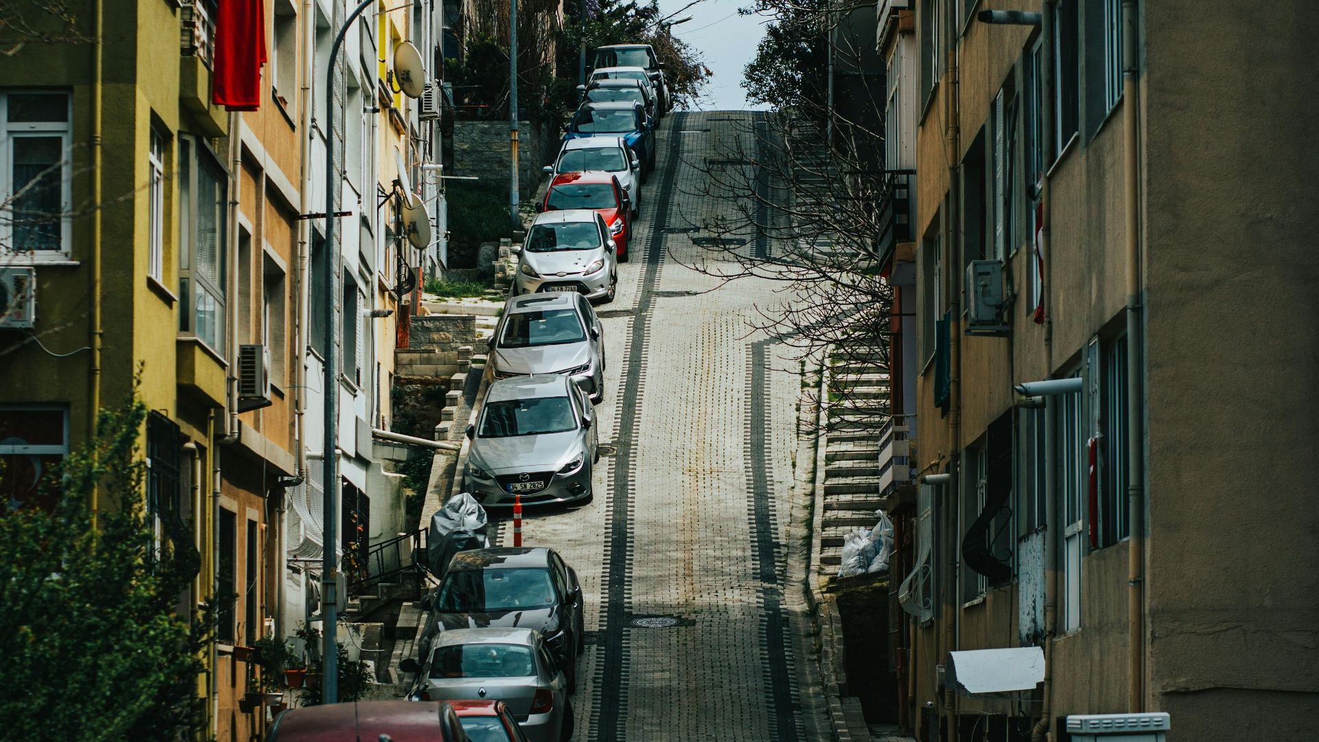 A steep urban street lined with parked cars and residential buildings, perfect for travel and architecture themes.
