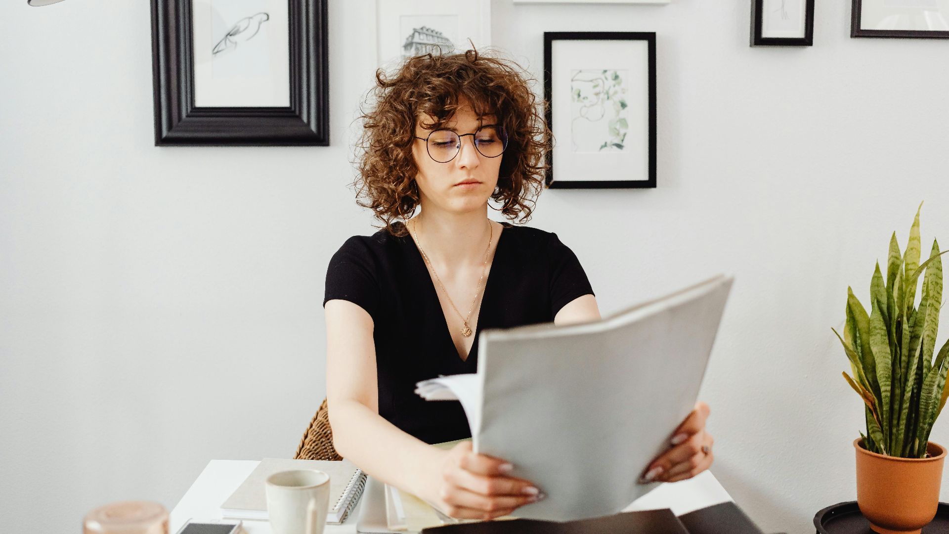 Woman with curly hair and eyeglasses reviewing documents at her desk.