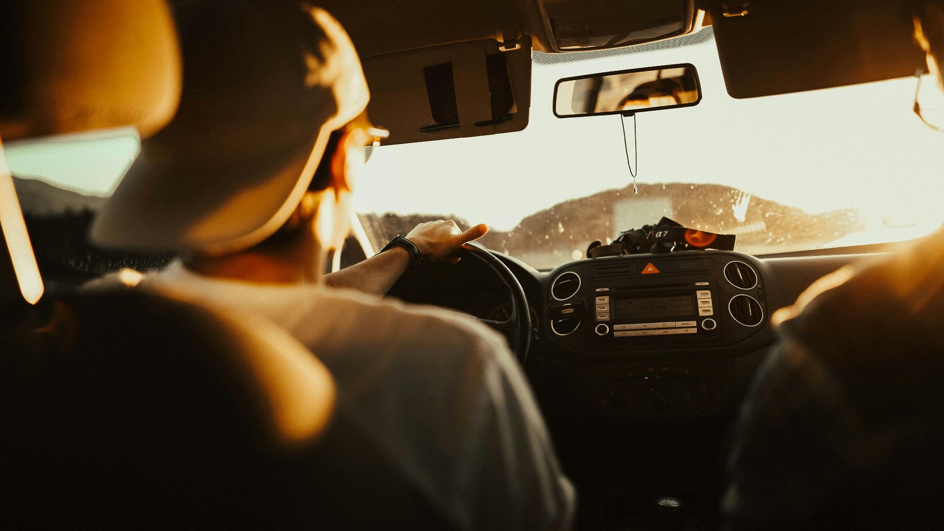 Man driving car with passenger at sunset, capturing warm sunlit atmosphere.