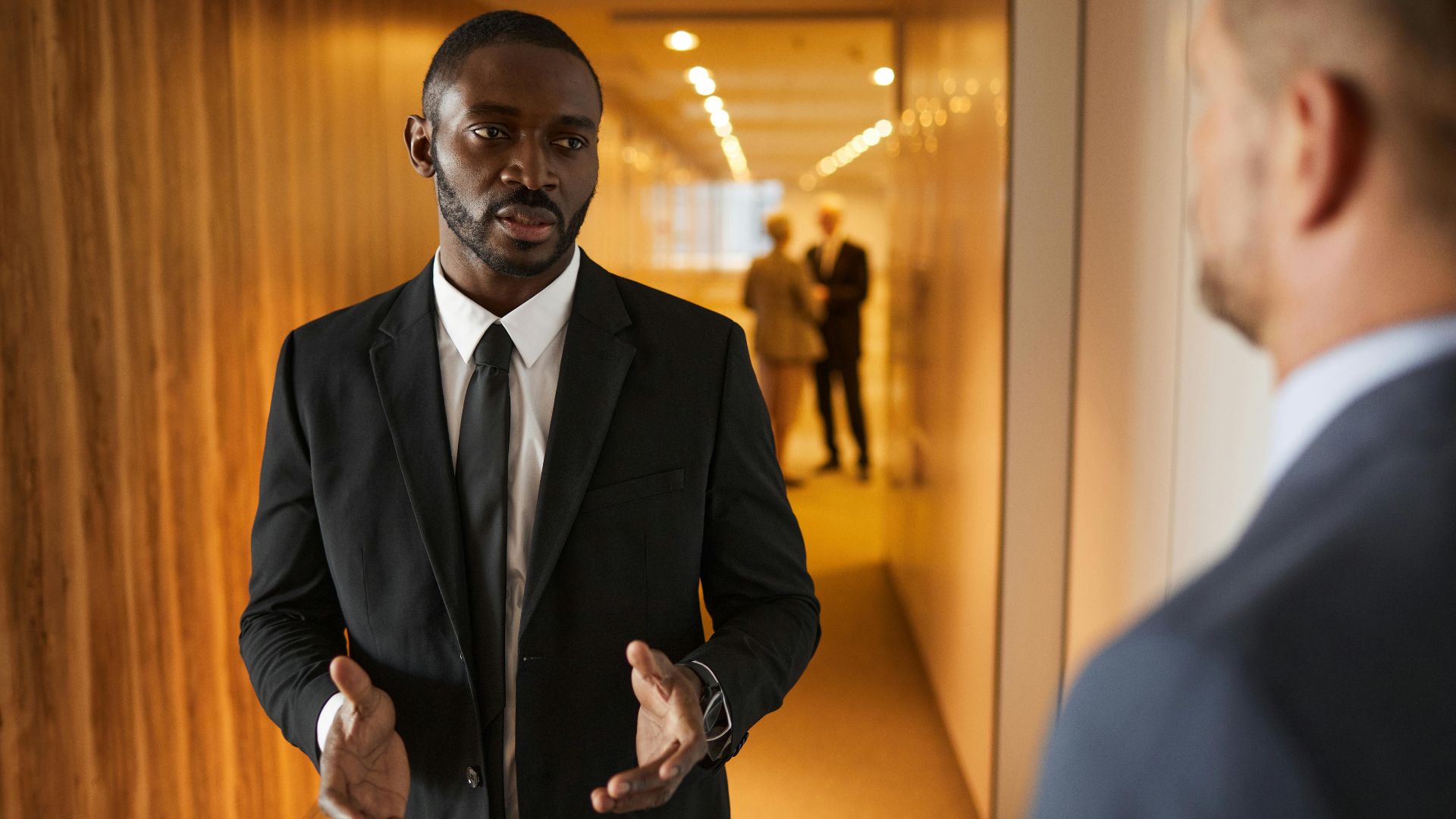 Business professionals in suits having a conversation in a modern office hallway.