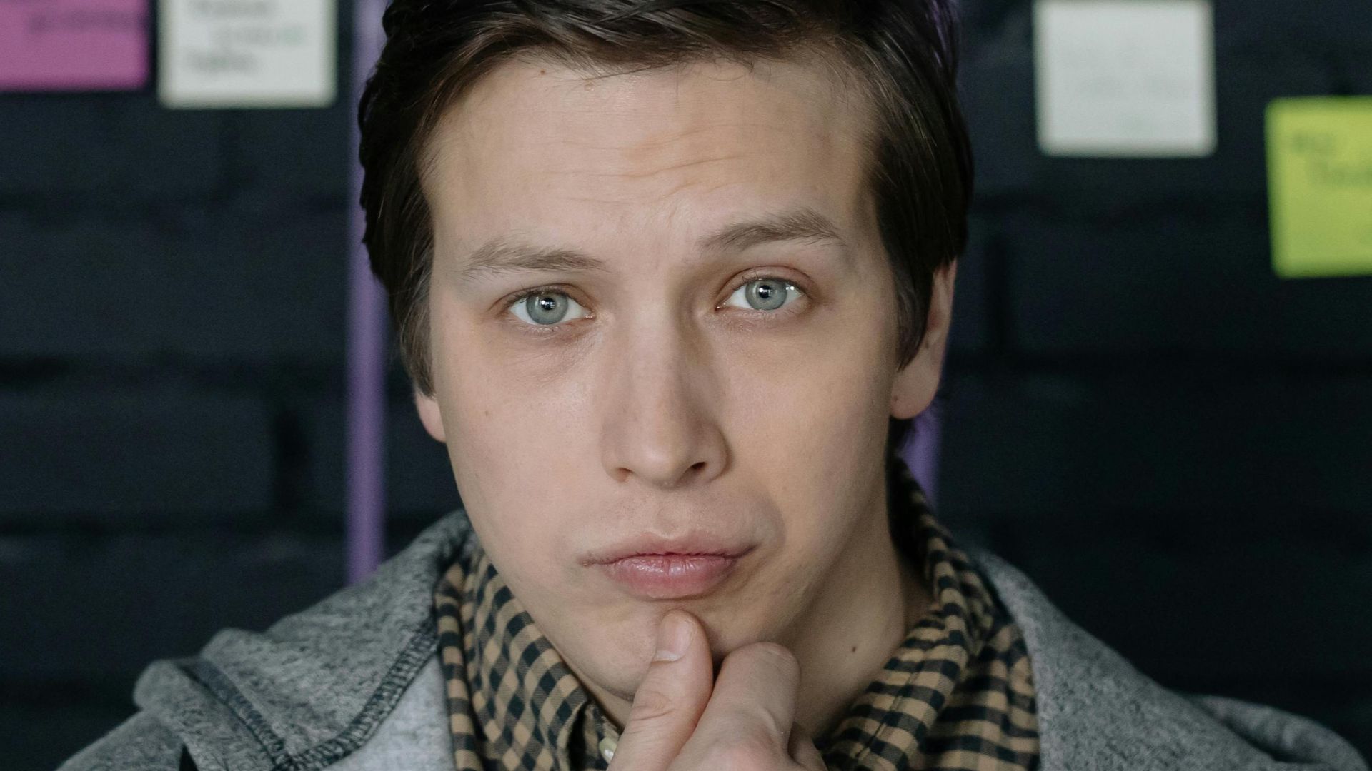 Thoughtful man pondering ideas in creative workspace with sticky notes behind.