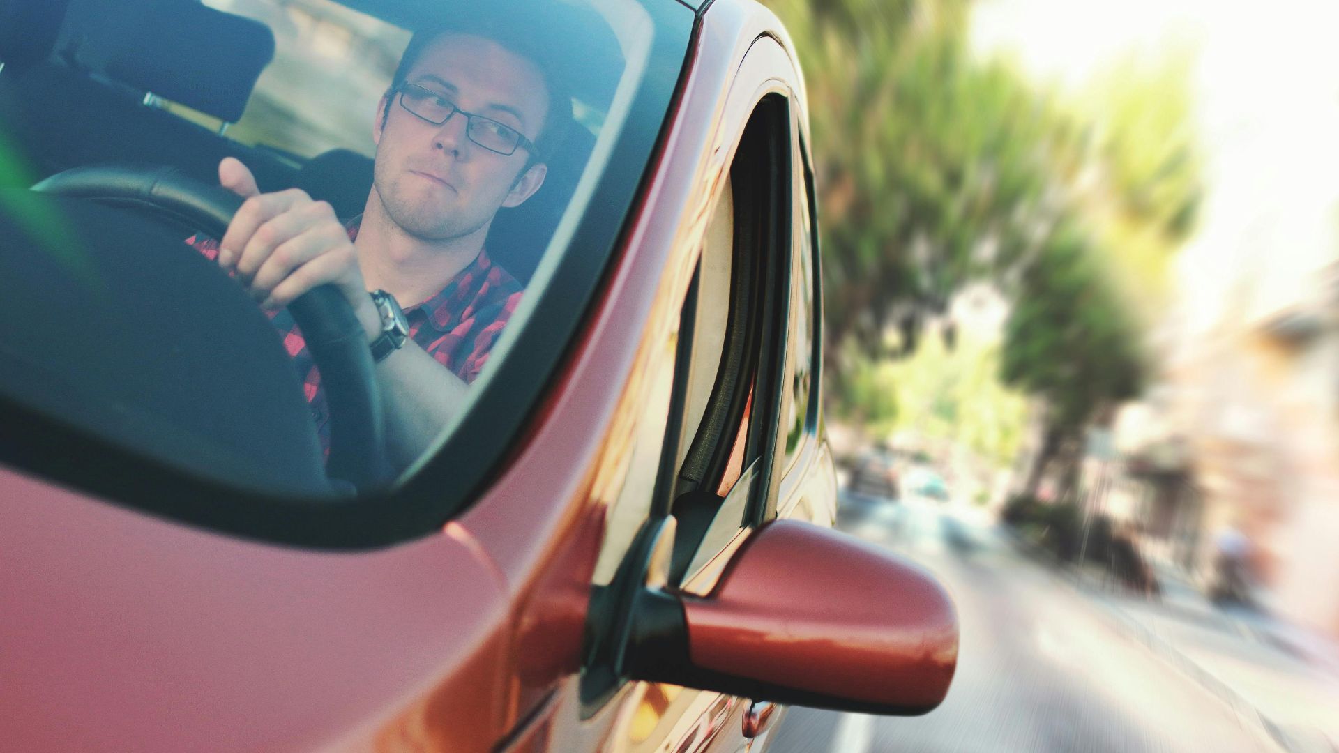 A man driving fast through a city street in a red car, showcasing motion and focus.