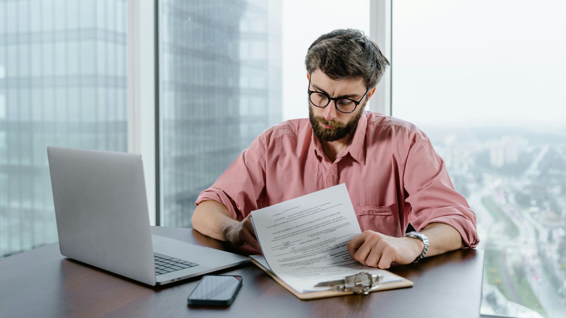 Professional man in pink shirt working with documents at a modern office desk.
