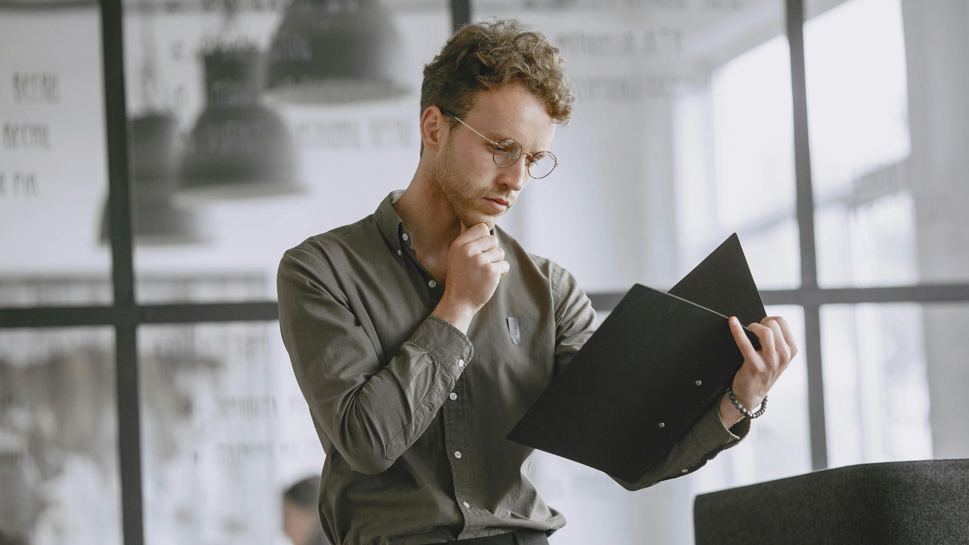 Business professional analyzing documents in a modern office setting, wearing eyeglasses.