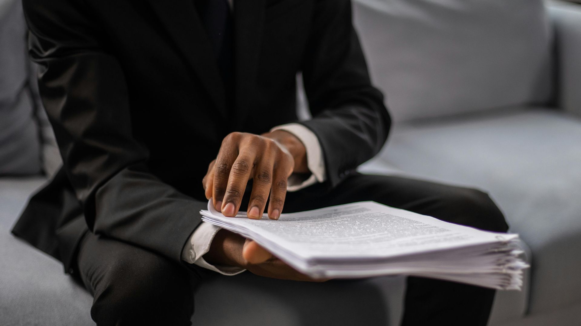 Close-up of a businessman in a suit reviewing documents while seated on a sofa indoors.